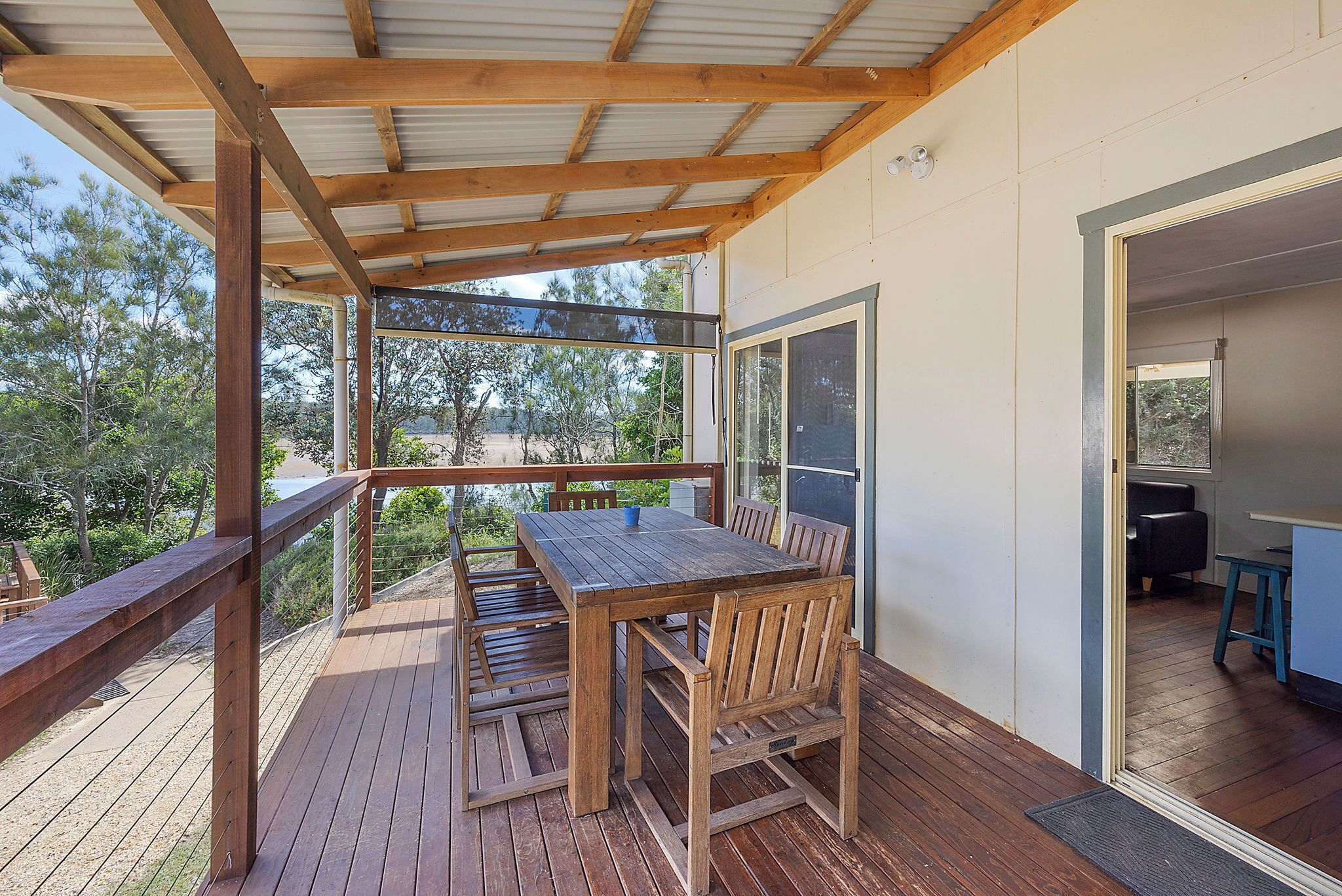A wooden deck with a table and chairs, a covered area with a metal roof, and a view of the outdoors.