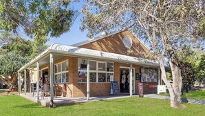 A brick building with a covered patio area, a signboard, and a tree in front. - Reflections Red Rock - Holiday Park (Red Rock)