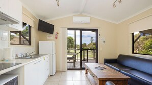 A compact kitchen with a built-in dishwasher, a dining area with a wooden table, and a blue leather sofa. - Reflections Red Rock - Holiday Park (Red Rock)