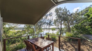 A wooden deck with a table and chairs, overlooking a body of water and trees. - Reflections Red Rock - Holiday Park (Red Rock)