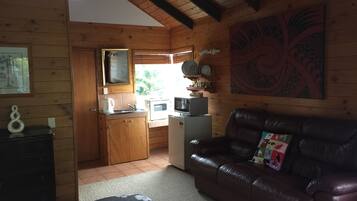 A cozy cabin-style room with a wooden interior, a kitchenette, a leather sofa, and a large window providing natural light.