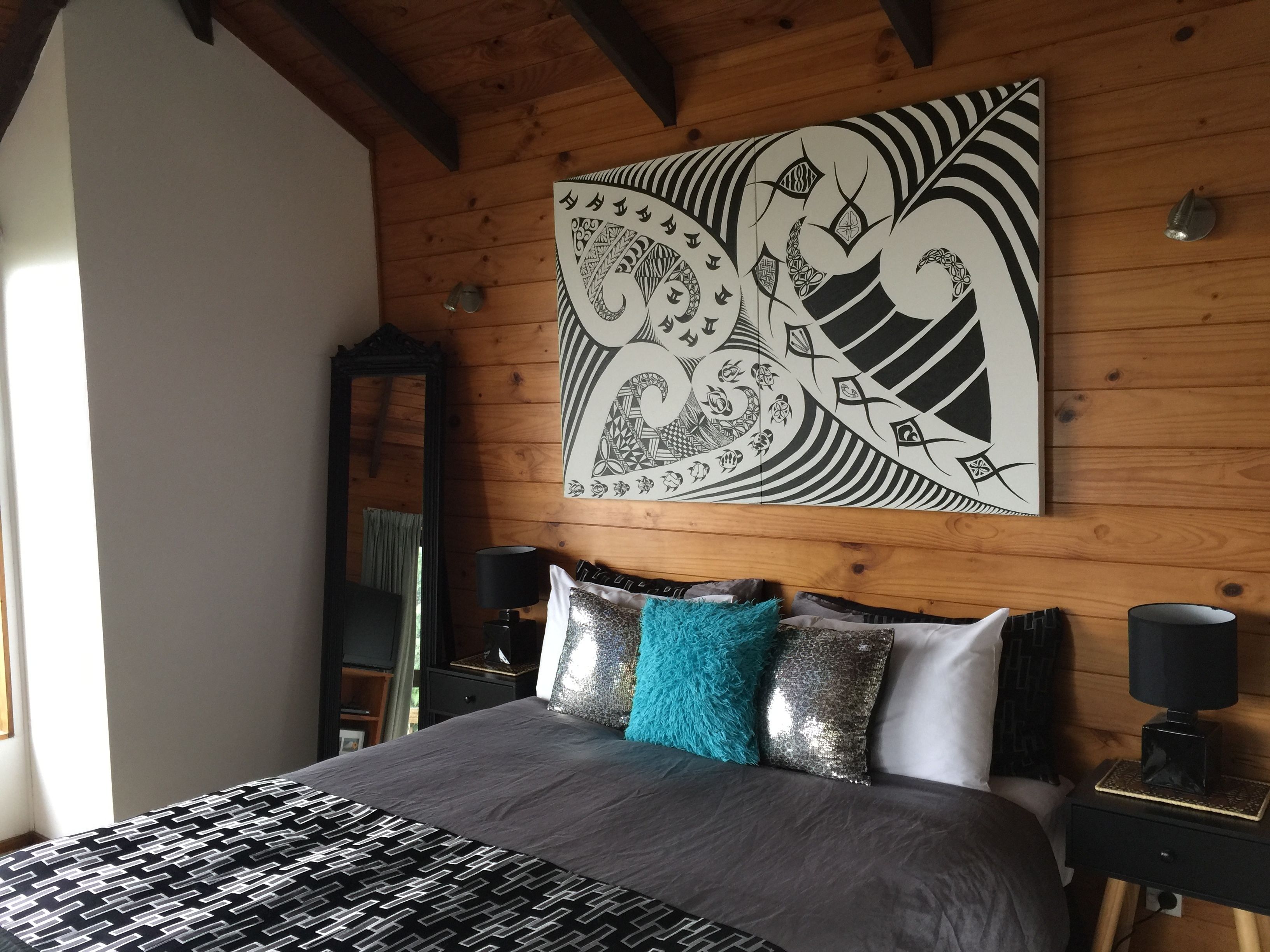 Un dormitorio con cama, techo de madera, una obra de arte grande en la pared y una mesita de noche con lámpara.