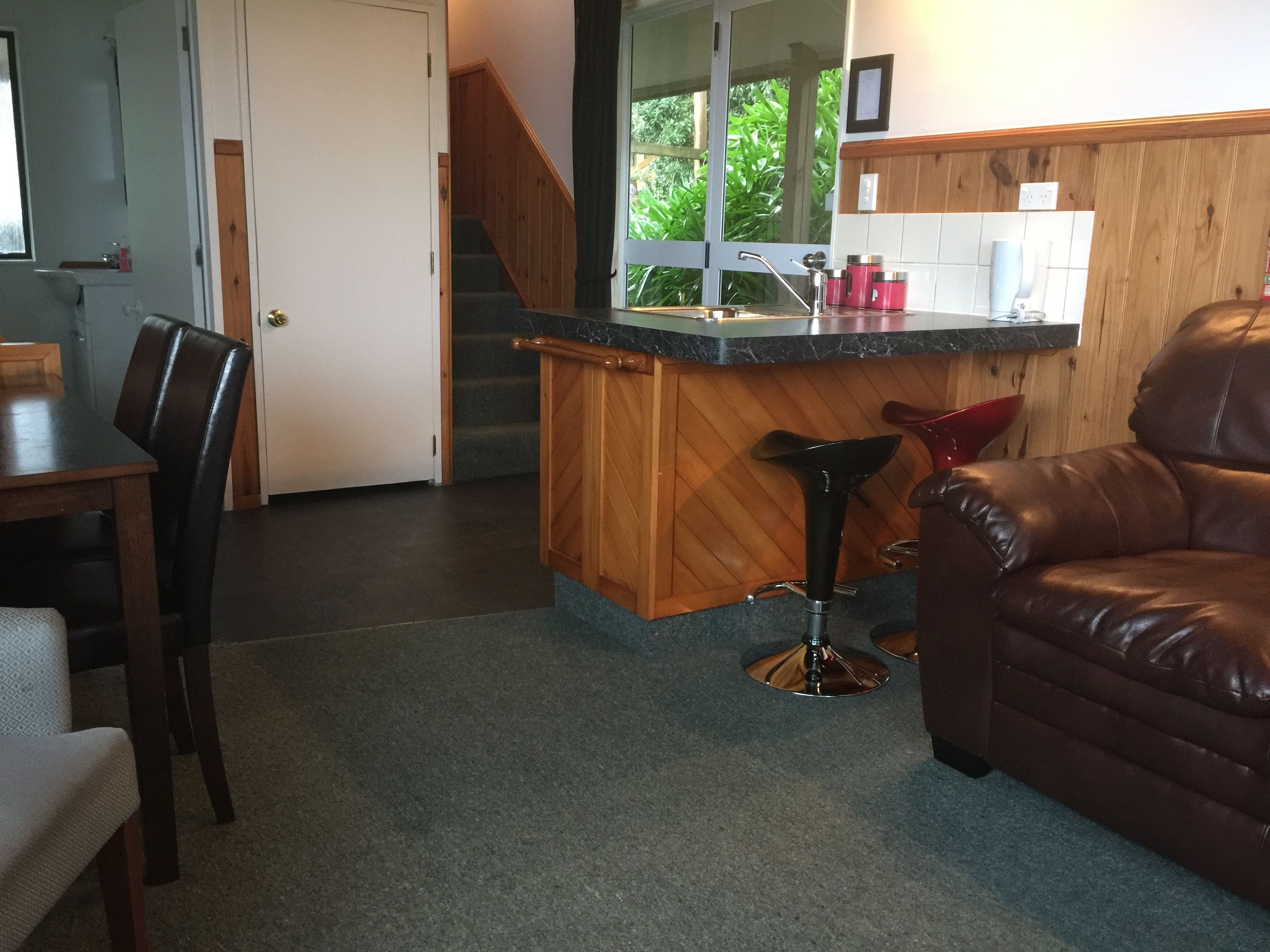 A kitchen with a wooden counter, a sink, and a bar stool. There is a dining table with chairs and a leather sofa.