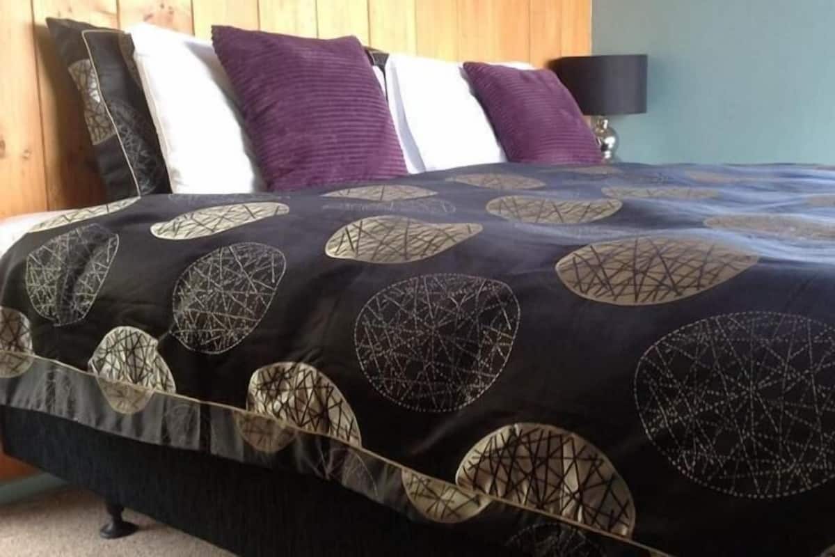 Una cama con un edredón de estampado blanco y negro, un cabecero de madera y una lámpara sobre una mesita de noche.