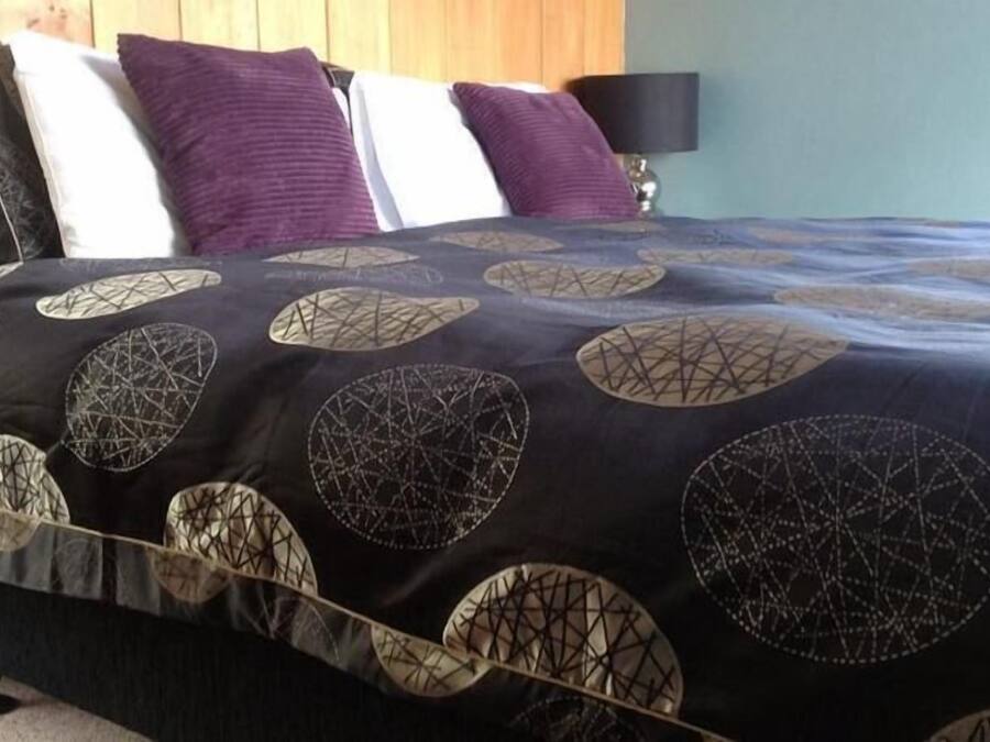 A bed with a black and white patterned bedspread, a wooden headboard, and a lamp on a bedside table.