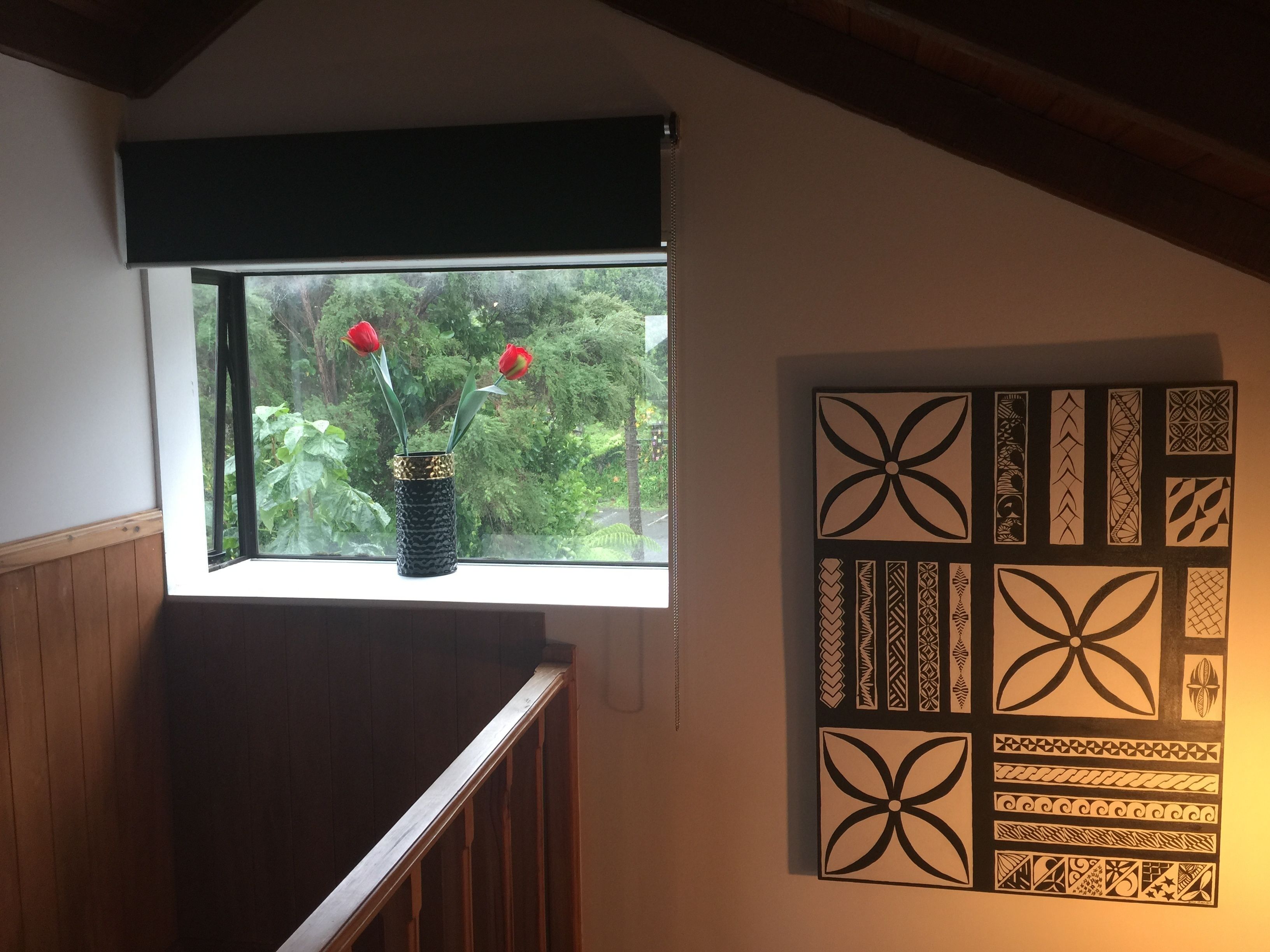 A room with a window overlooking greenery, a wooden railing, and a wall with decorative patterns.