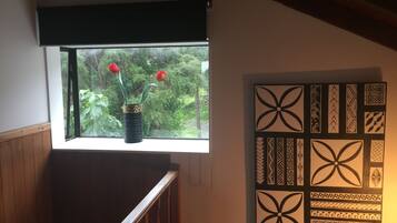 A room with a window overlooking greenery, a wooden railing, and a wall with decorative patterns.