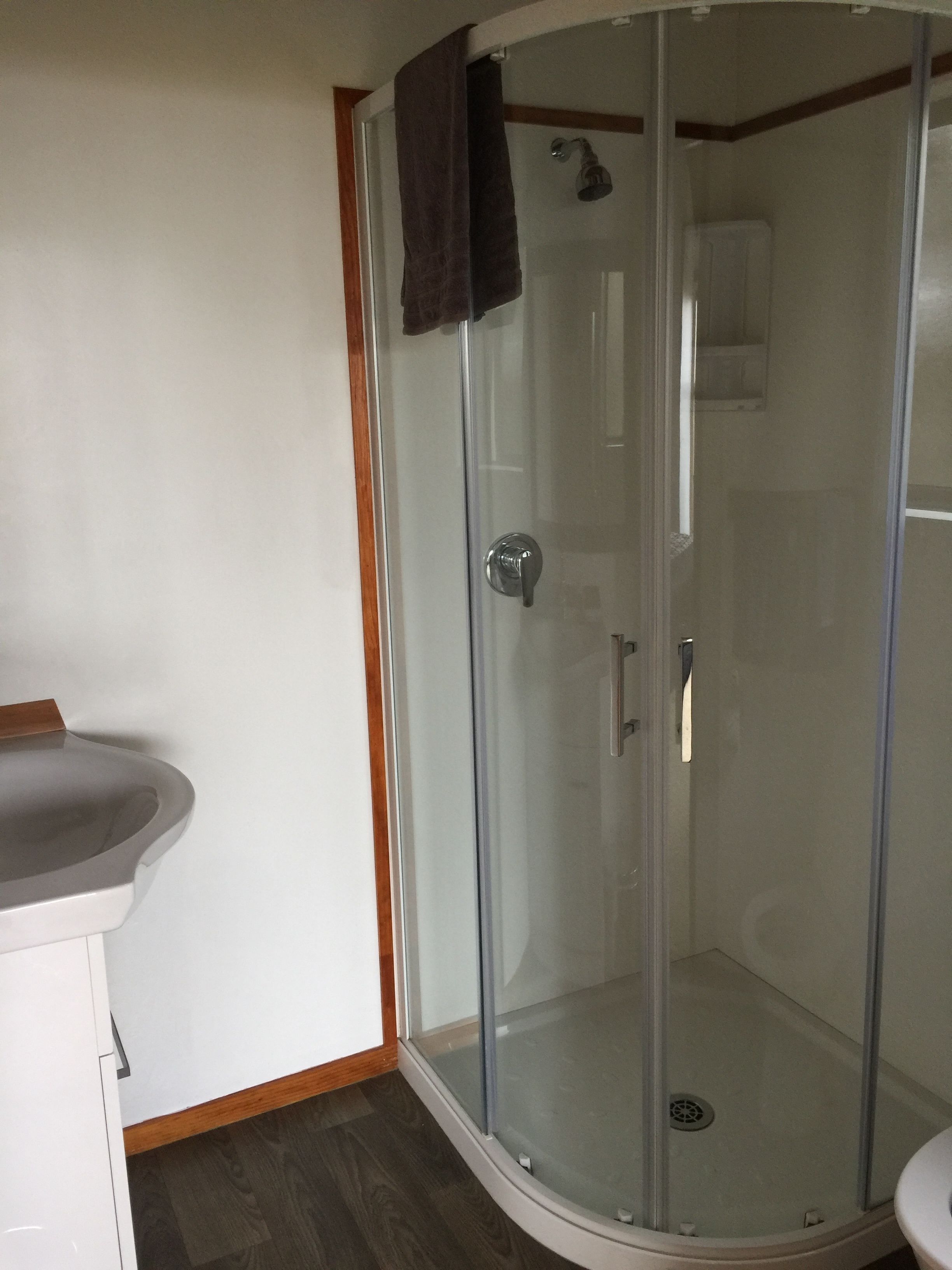 A glass-enclosed shower with a white sink and wooden trim.