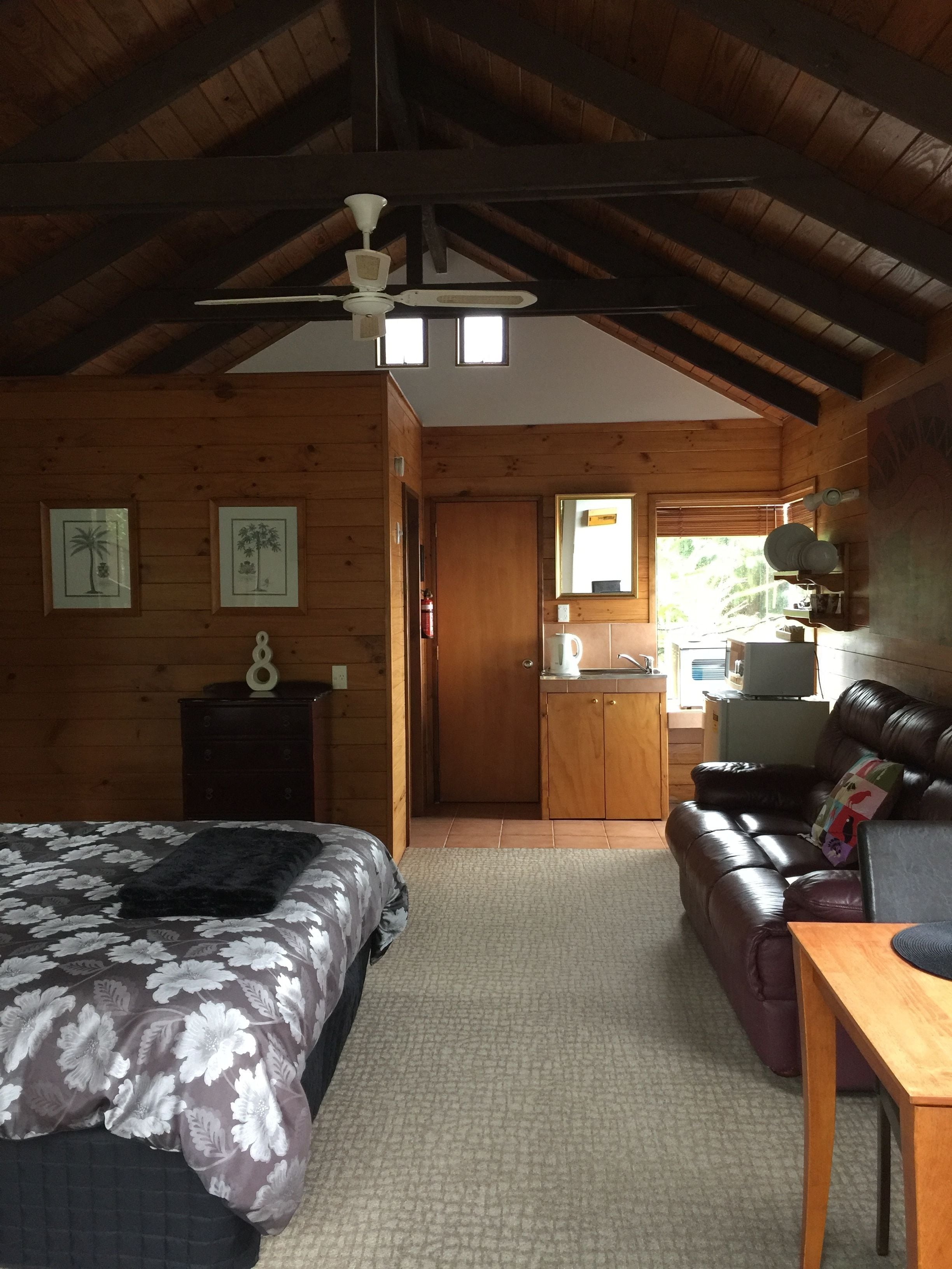 A cozy cabin with a wooden interior, a bed with a floral bedspread, a leather sofa, and a kitchenette in the background.