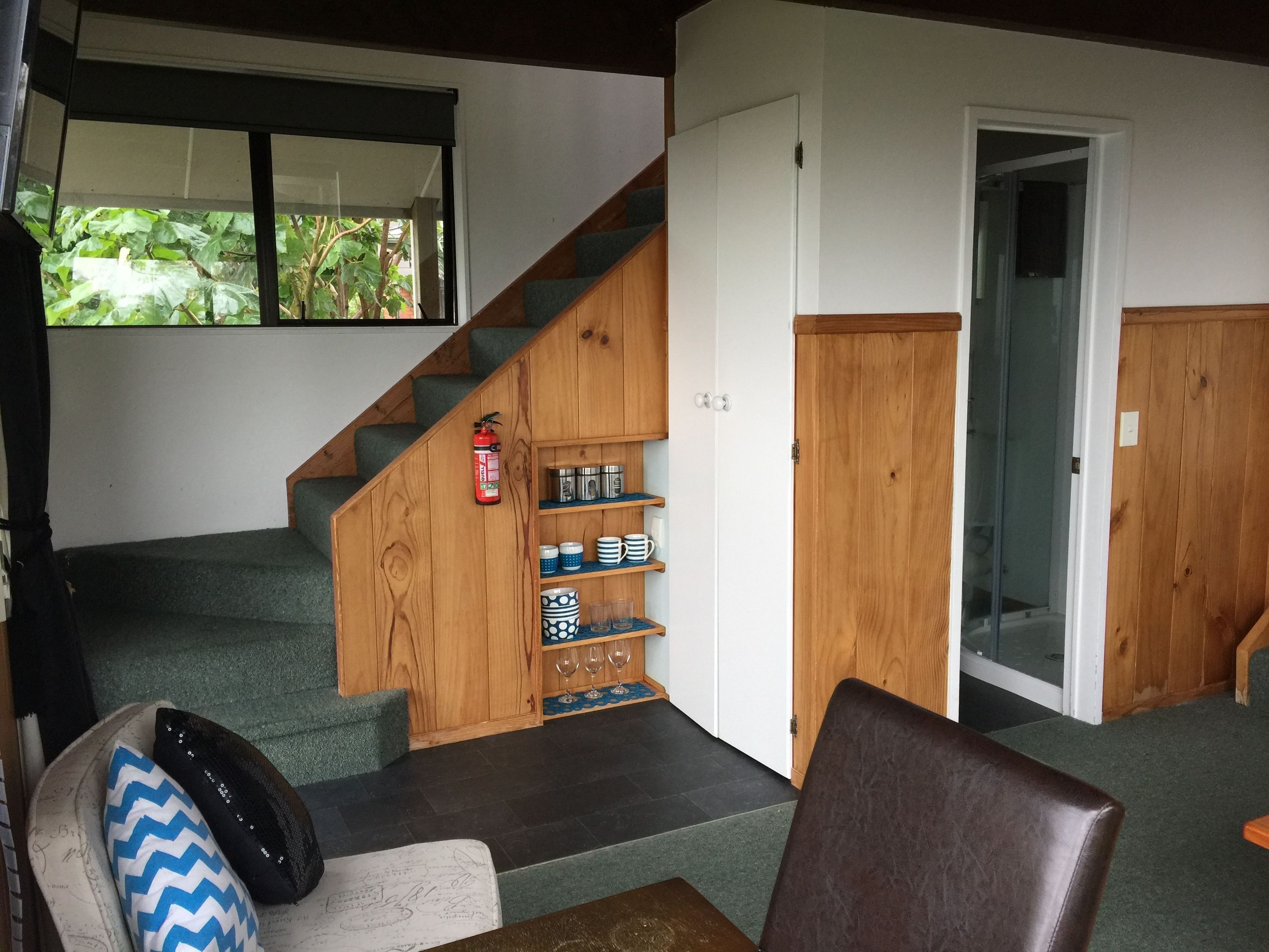 A staircase with a wooden finish, a fire extinguisher, and a shelf with cups and glasses.