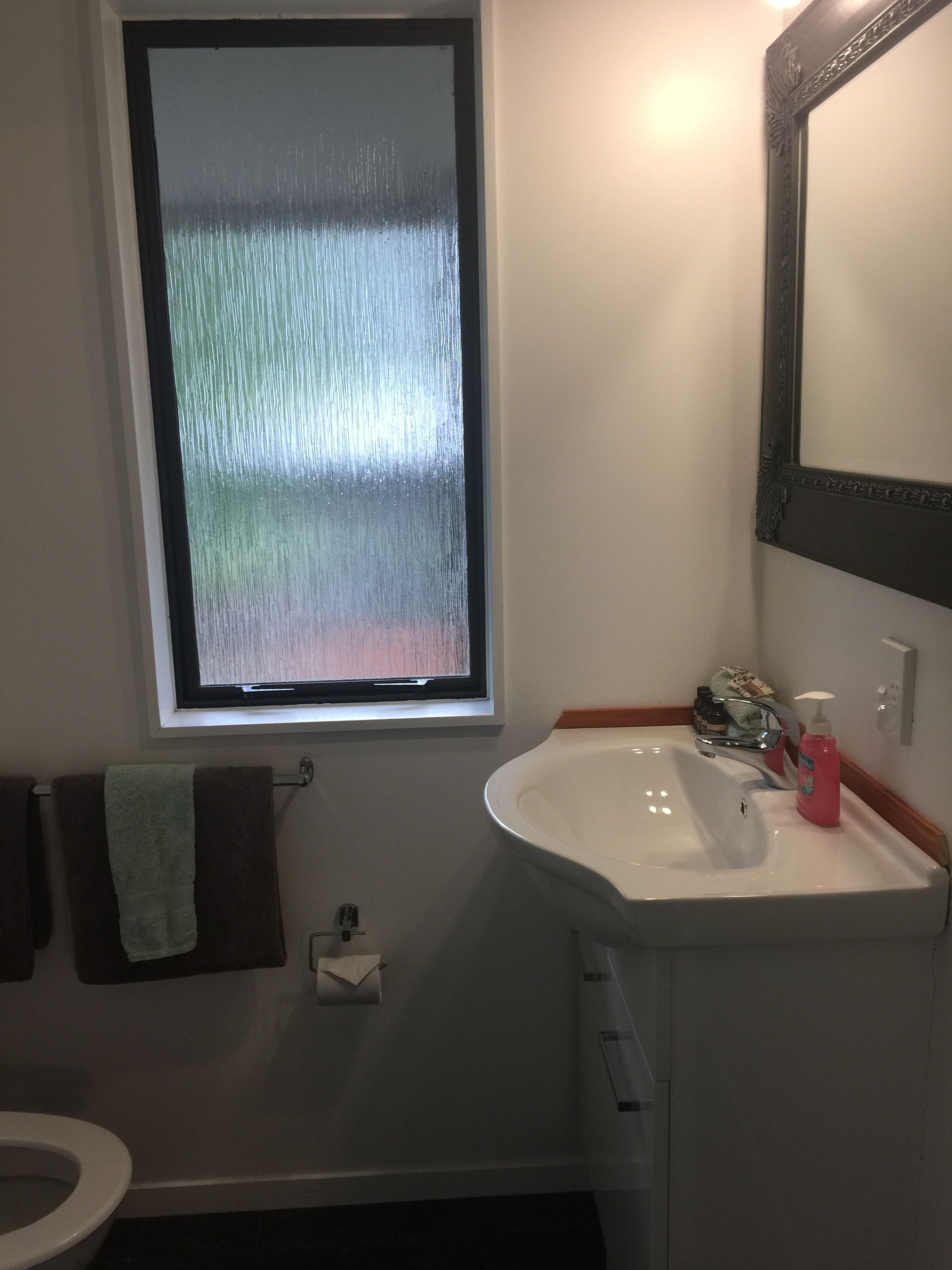 Une salle de bain avec une fenêtre, un lavabo, un miroir et un porte-serviettes.