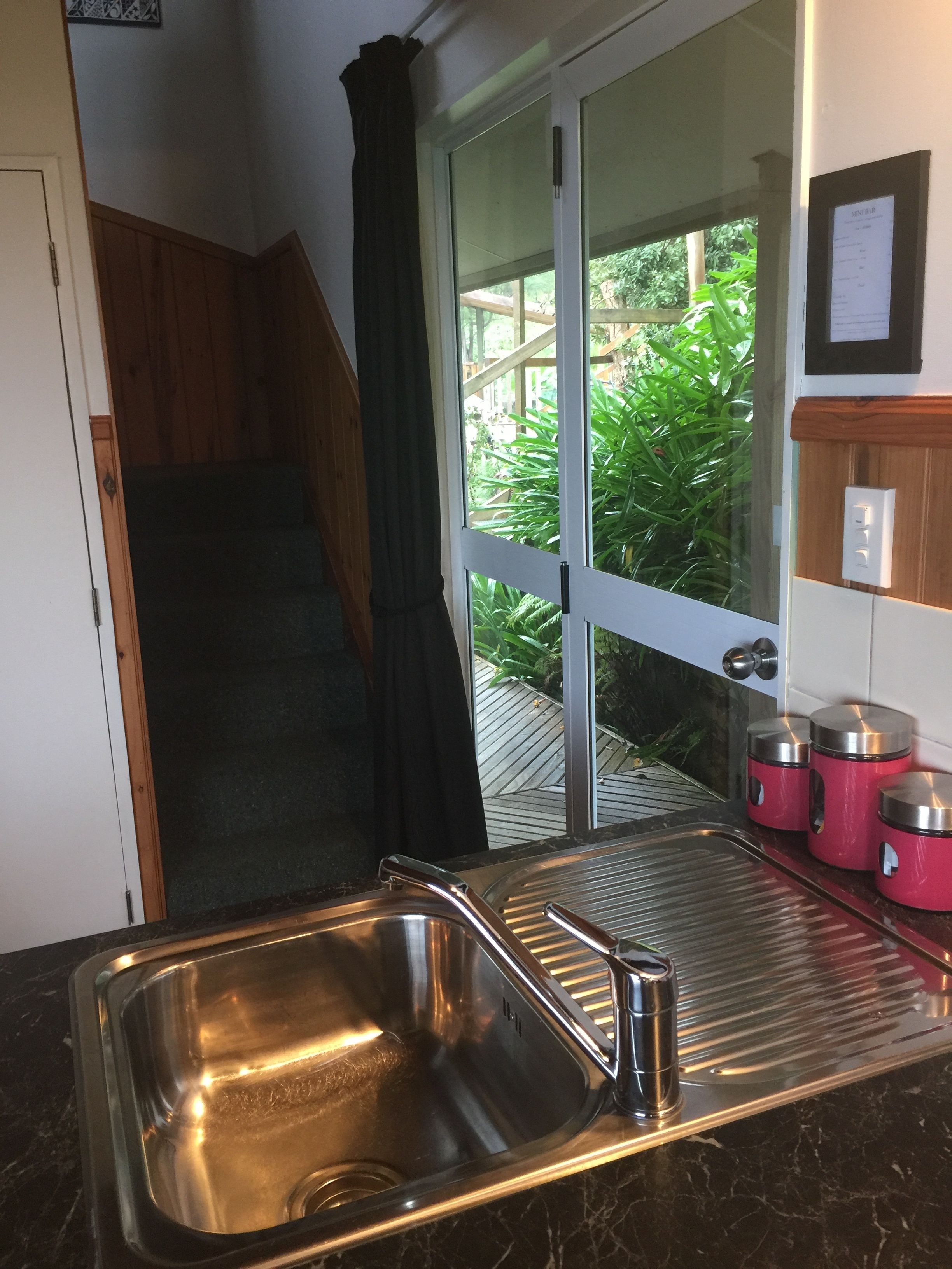 A kitchen with a stainless steel sink, a wooden staircase, and a sliding glass door leading to a garden.