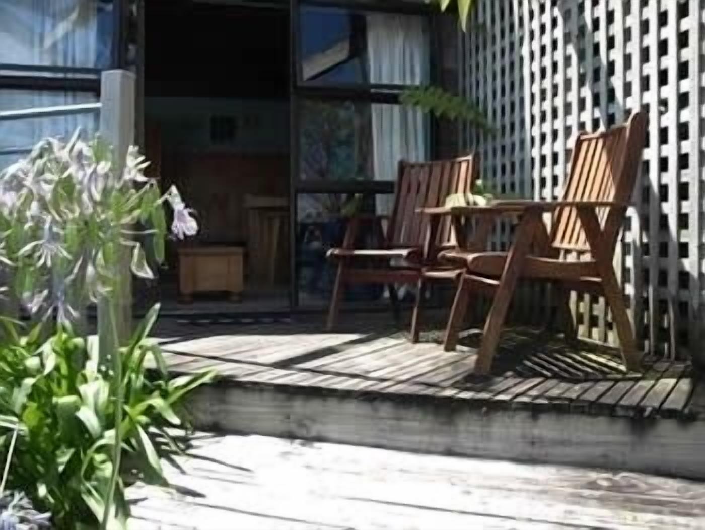 An outdoor seating area with wooden chairs and a table, surrounded by a wooden deck and a white fence.