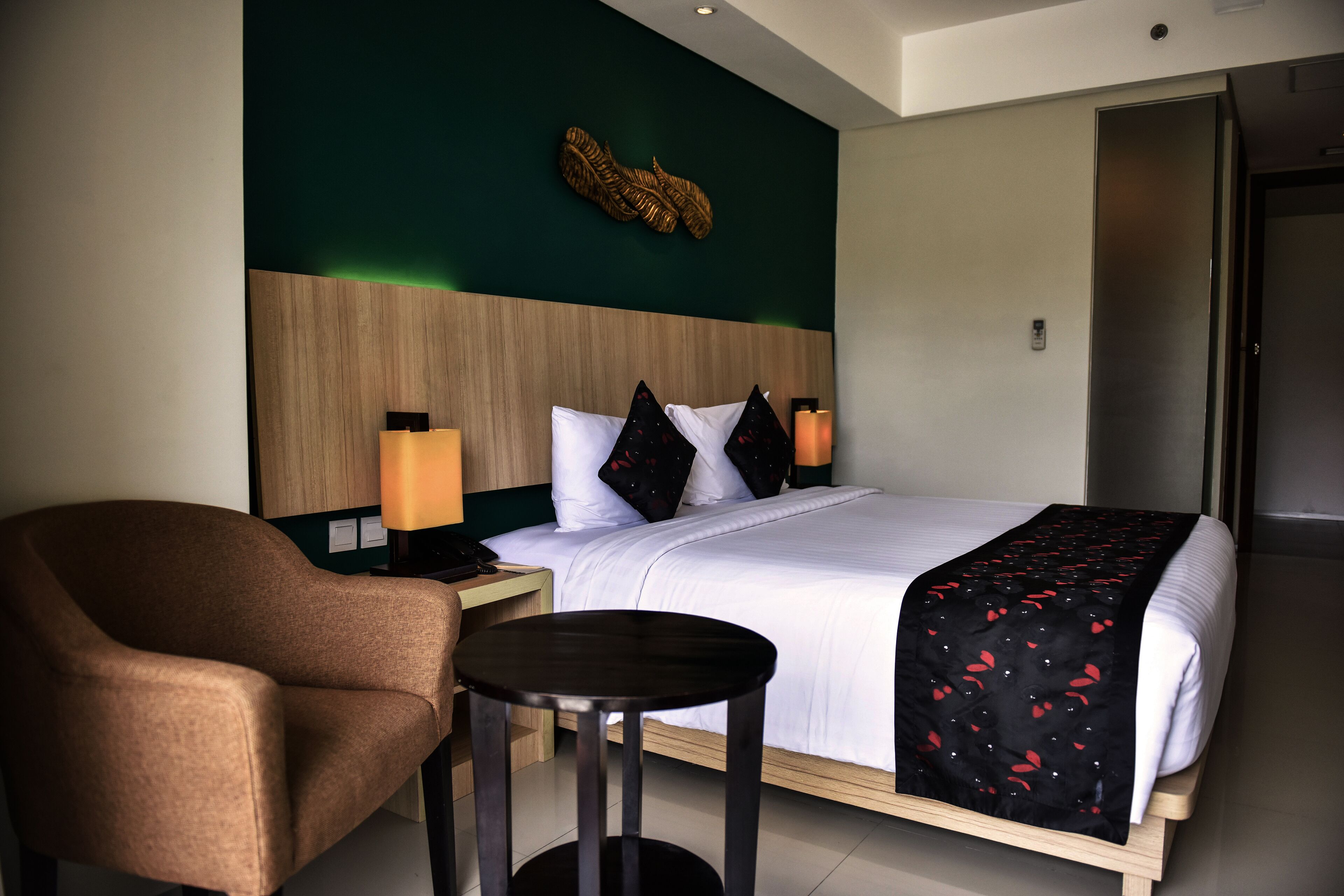 Ein Hotelzimmer mit einem Bett, einem Sessel, einem kleinen Tisch und einem Nachttisch mit Lampe.