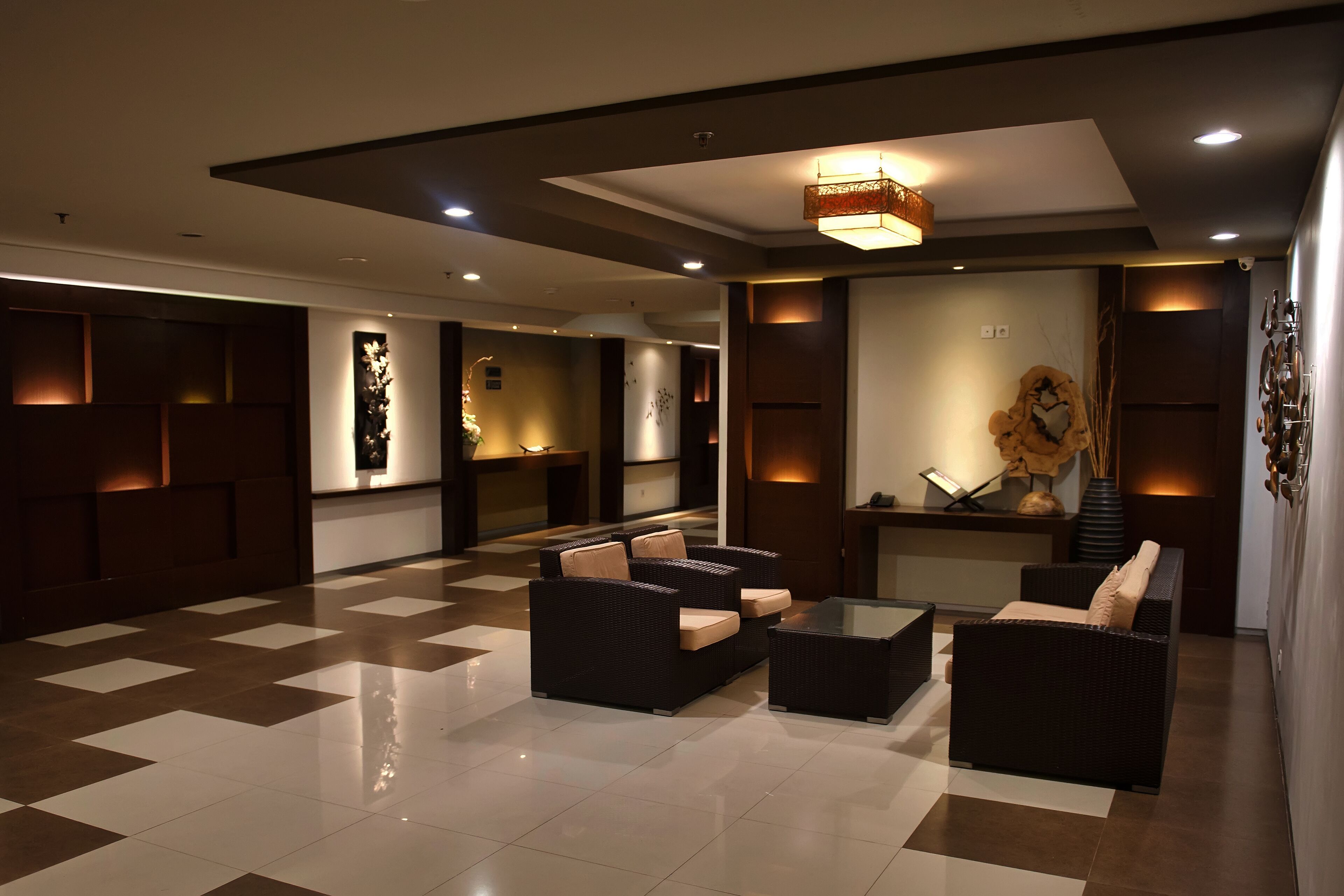 A modern lobby with black wicker sofas, a glass coffee table, and a decorative wall piece.
