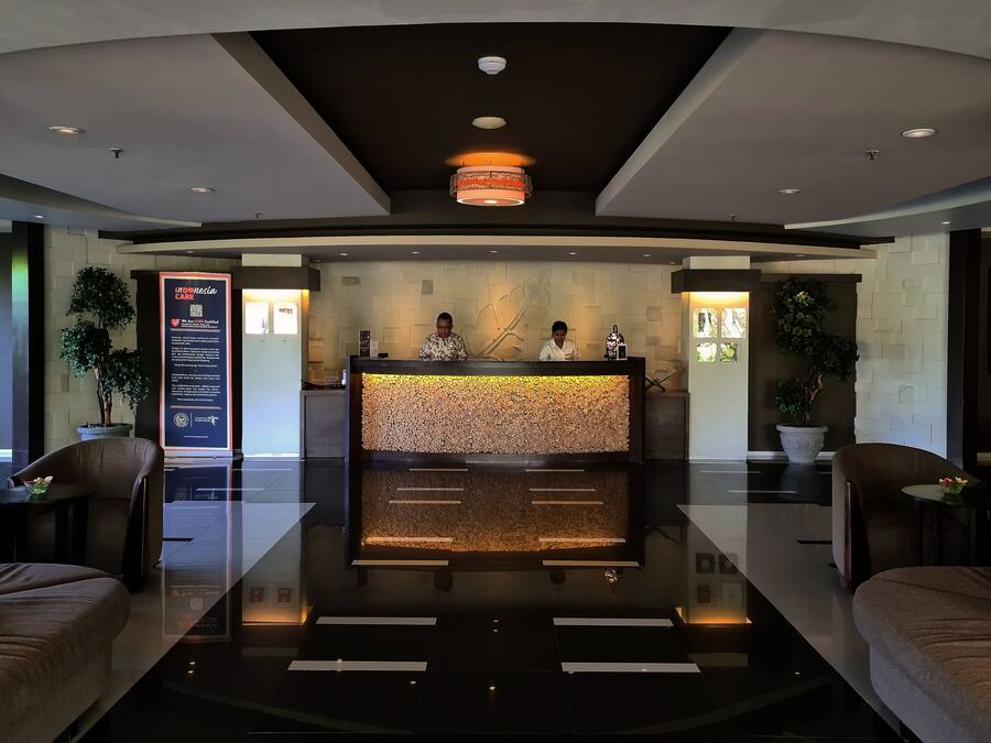 A modern reception area with a polished reception desk, two staff members, and a large informational sign.