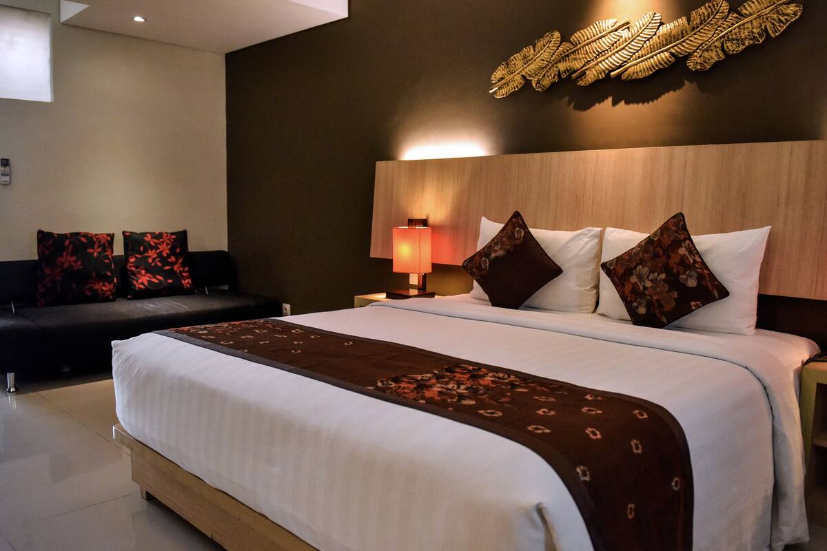 Una camera d'albergo con un letto grande, un comodino con una lampada, un divano e un elemento decorativo a parete.
