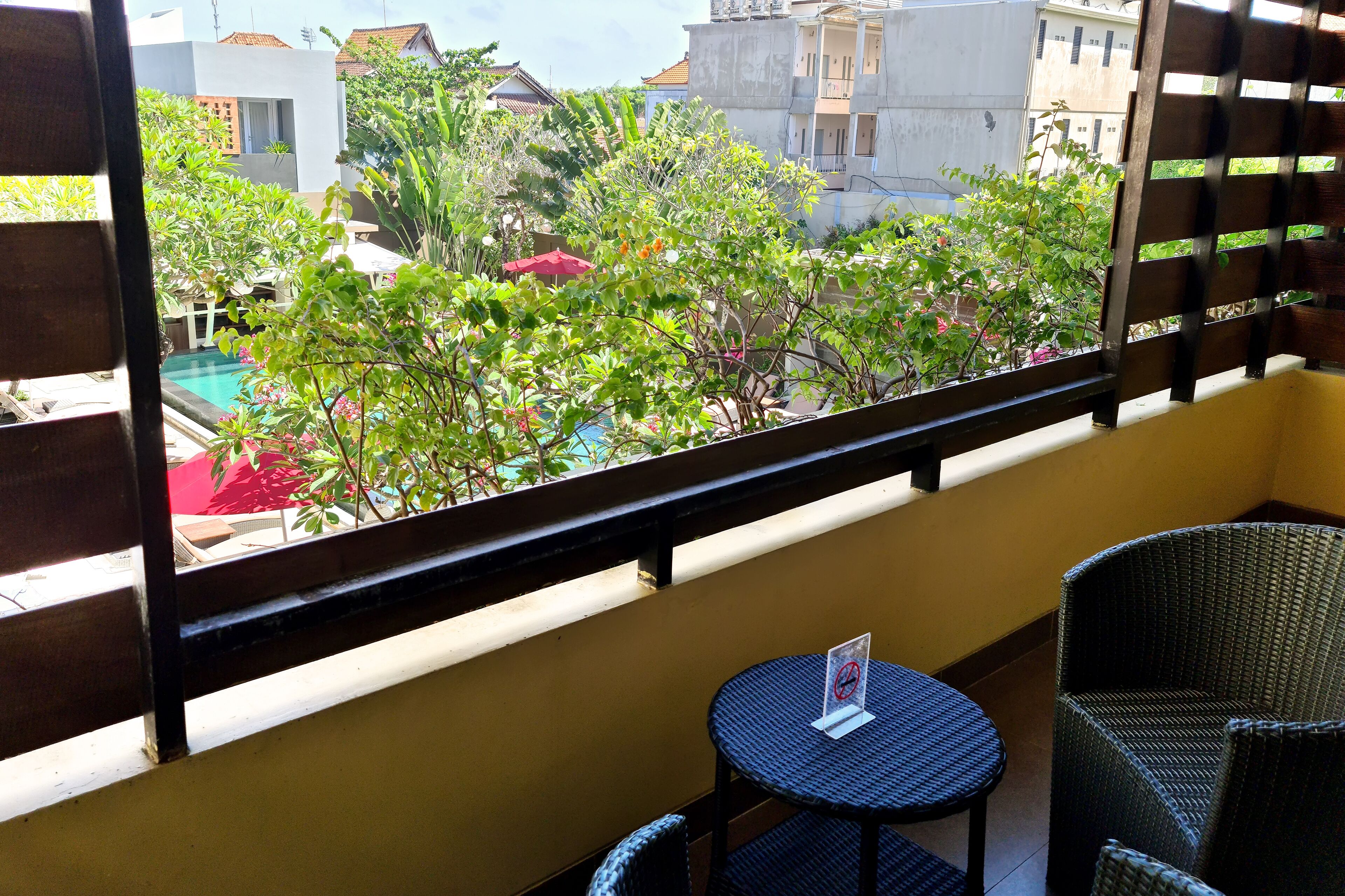 Un balcon donnant sur une piscine et un espace verdoyant, agrémenté de meubles en osier et d’une petite table.
