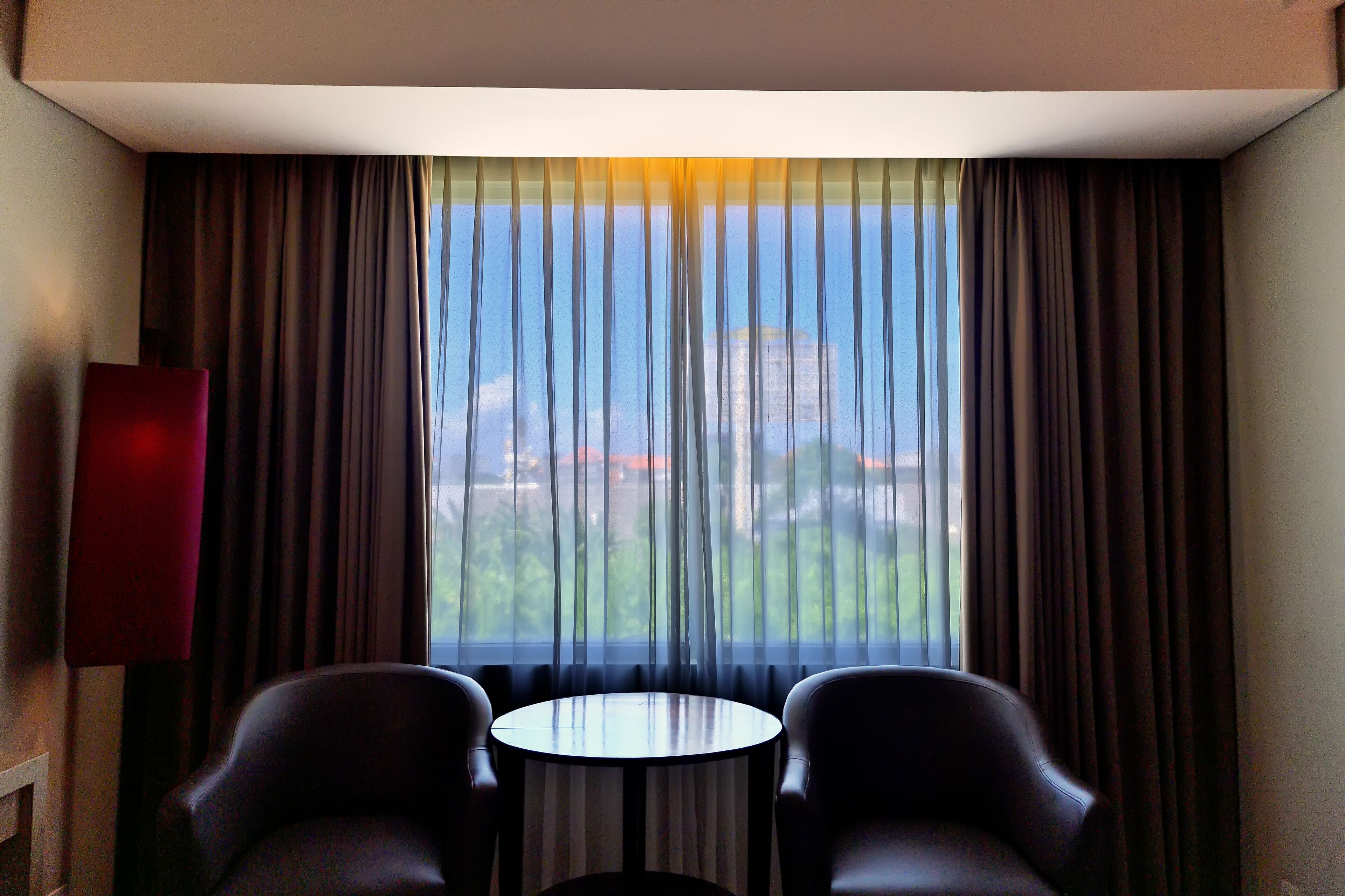A hotel room with a large window, two chairs, and a small round table.