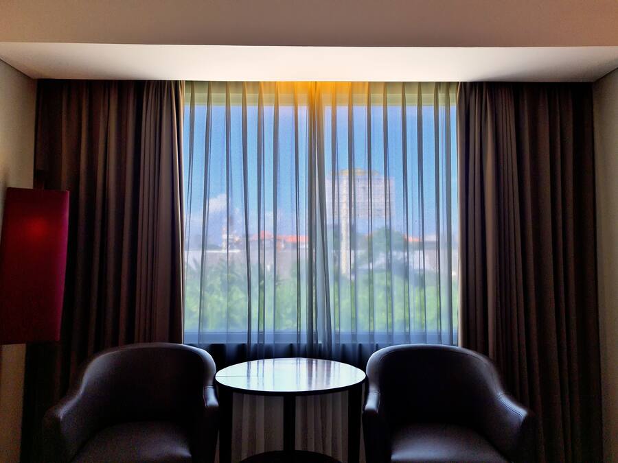Ein Hotelzimmer mit großem Fenster, zwei Stühlen und einem kleinen runden Tisch.
