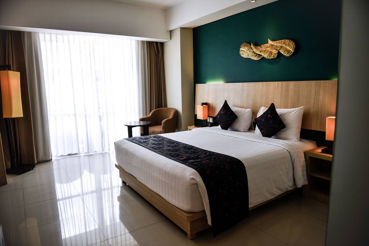 Una camera d'hotel con un letto grande, una testiera in legno, un elemento decorativo a parete e vista sull'esterno attraverso una finestra.
