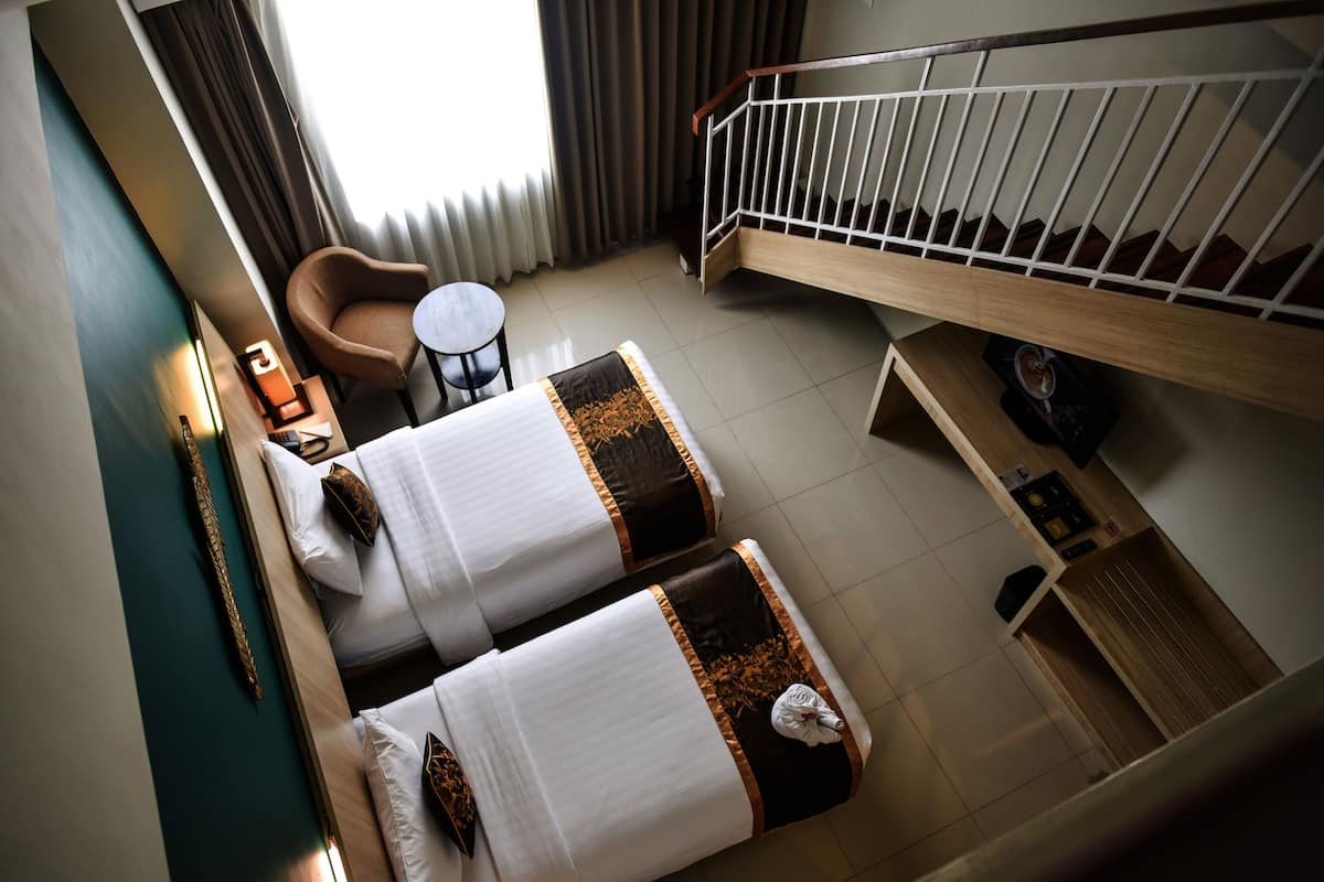 Camera d'albergo con due letti, una sedia, un tavolino, una panca di legno e una scala.