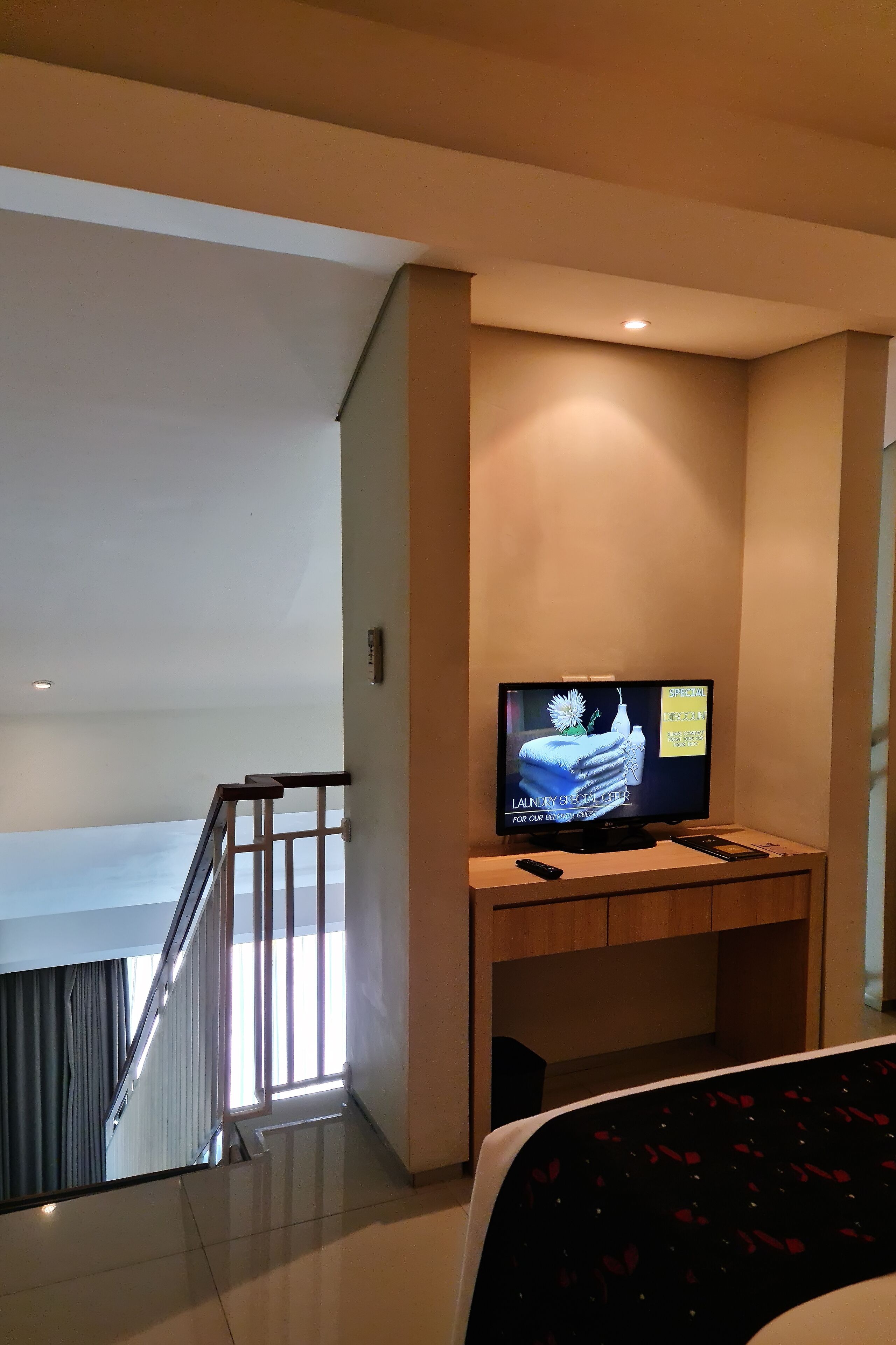 A hotel room with a television on a wooden stand, a remote control, and a bed with a patterned bedspread.
