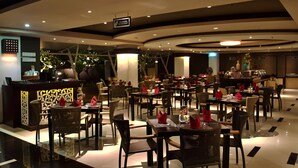 A modern restaurant with multiple dining tables and chairs, a bar area, and a sign indicating it is part of a hotel. - The Kana Kuta (Kuta)