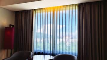 A hotel room with a large window, two chairs, and a small round table.