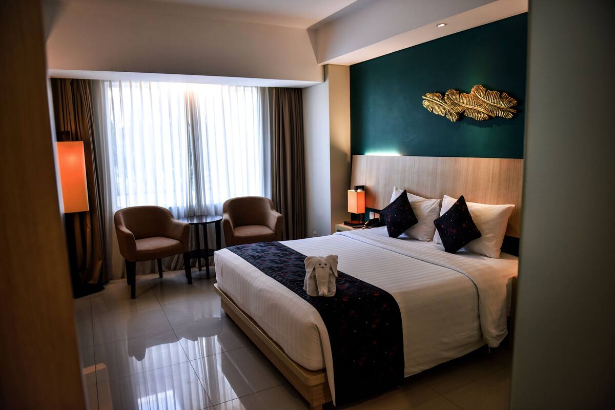 Una camera d'albergo con un letto grande, due poltrone, una scrivania e un elemento decorativo a parete.