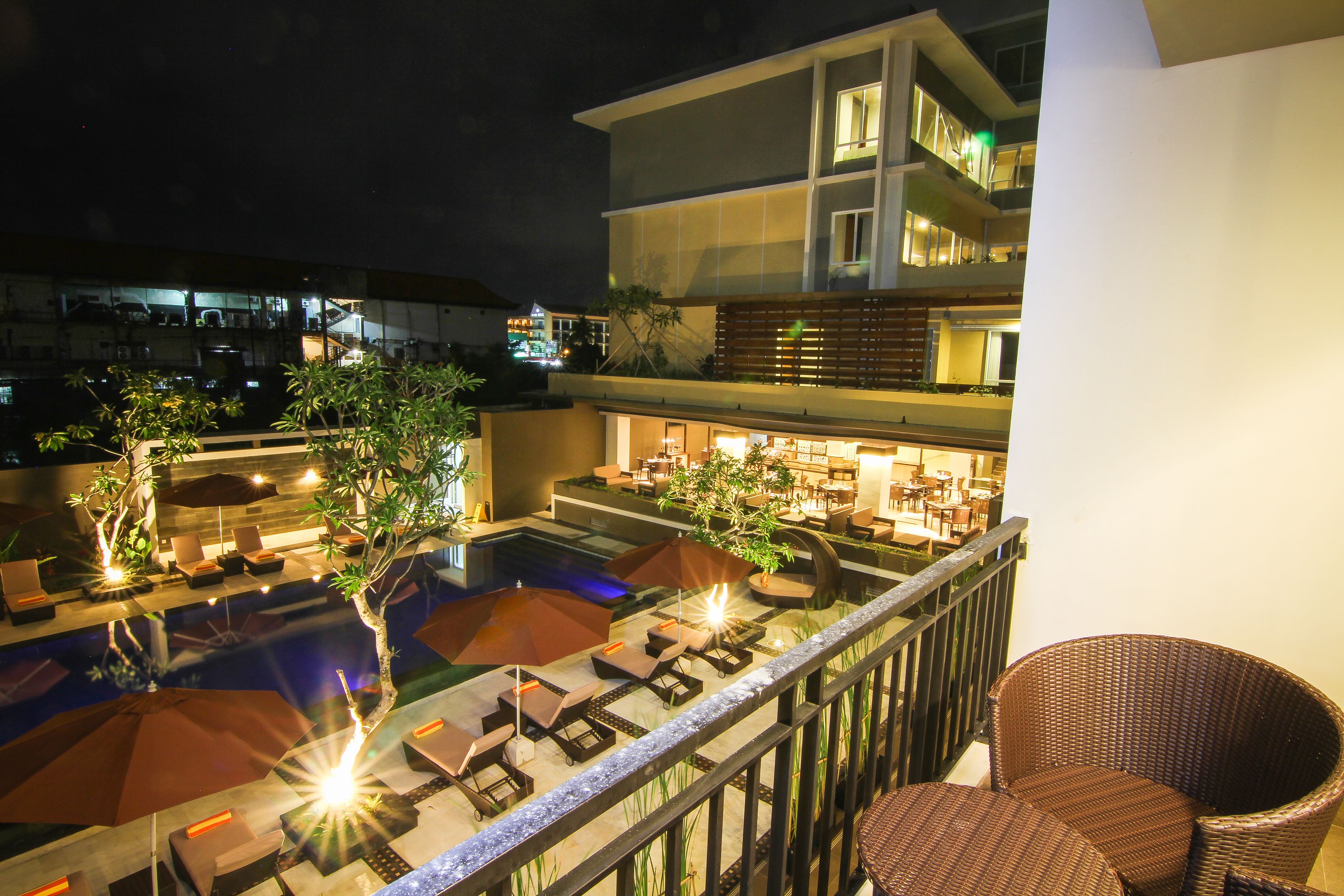 A rooftop pool area with lounge chairs and umbrellas, a bar, and a staircase leading to an upper level.