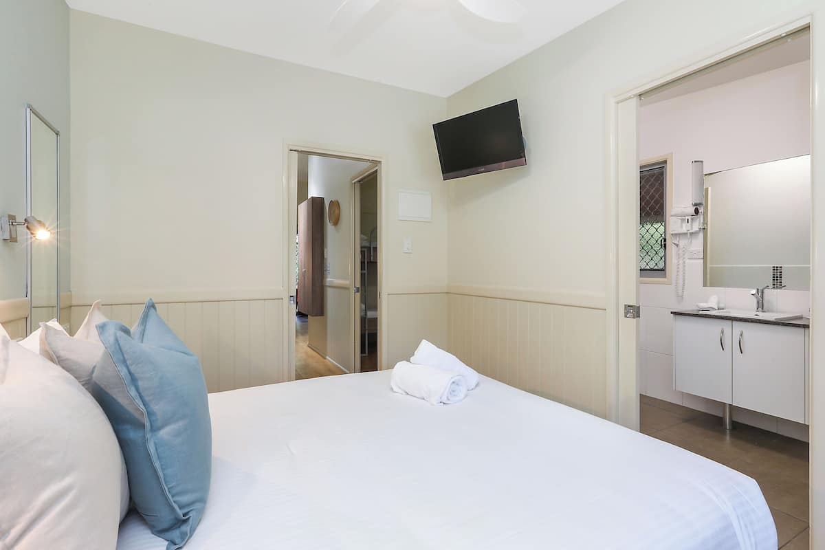 Een hotelkamer met een bed, een televisie, een badkamer met een wastafel en spiegel, en een deur die naar een andere kamer leidt.