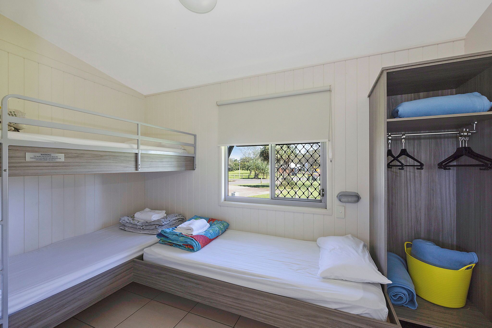 Una habitación pequeña con una cama individual y una litera superior, una ventana con vistas y un armario con perchero.