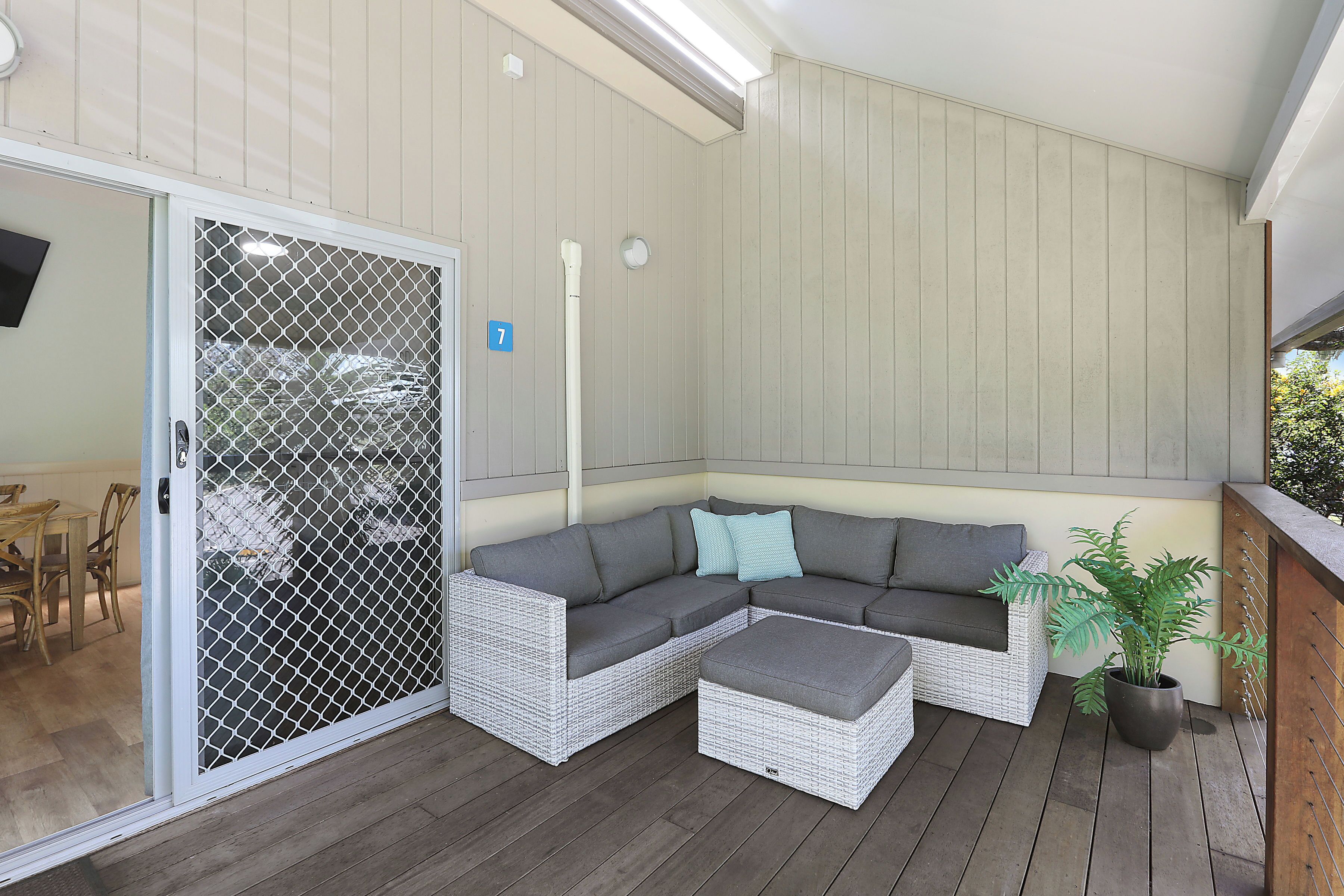 A covered patio area with a sectional sofa, a small ottoman, and a potted plant.