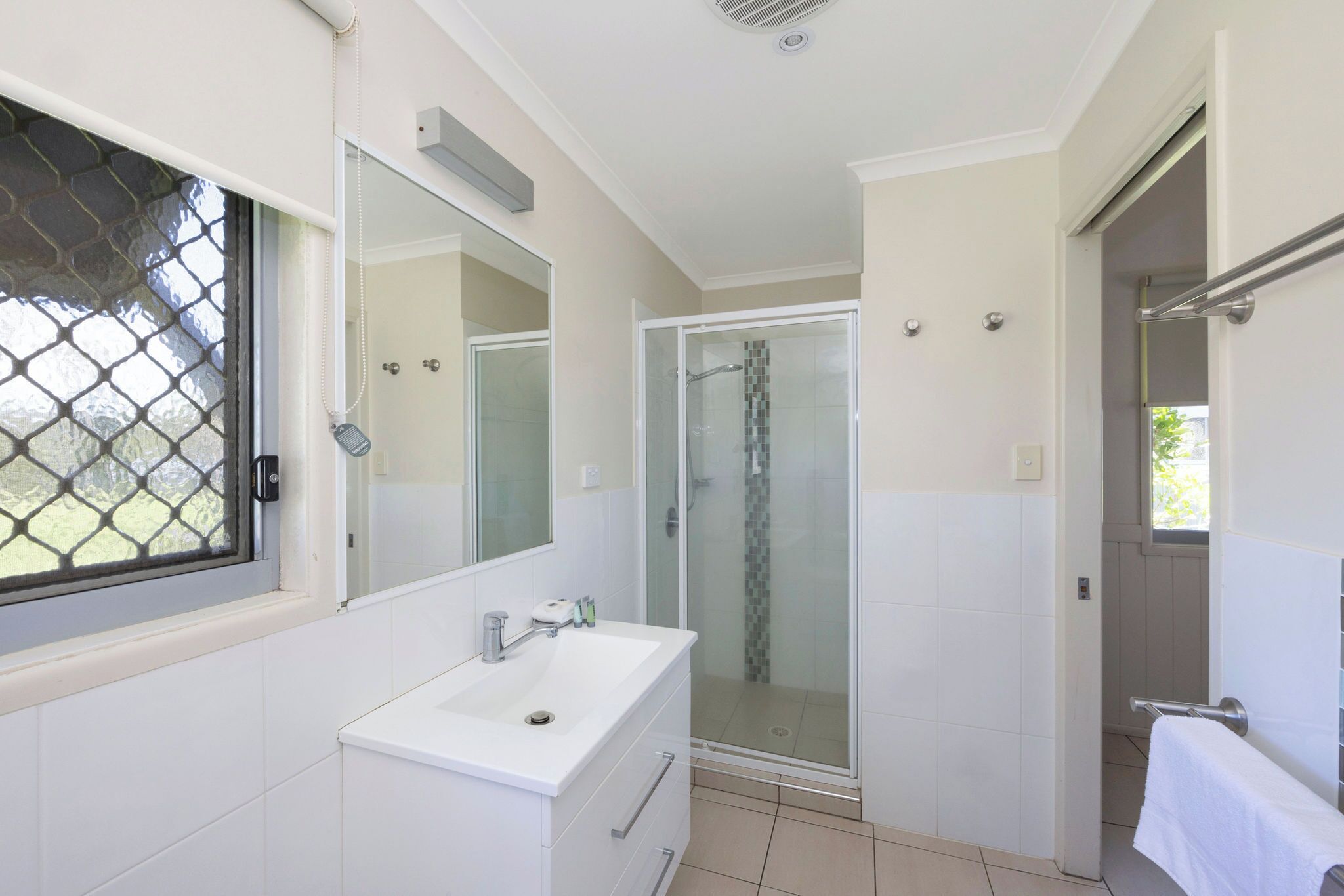A modern bathroom with a white sink, a glass shower enclosure, and a large mirror.