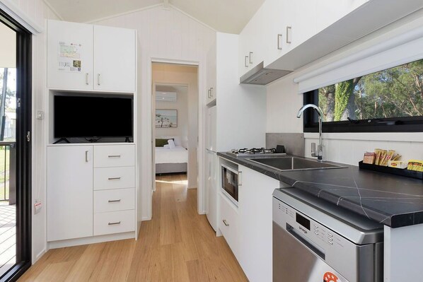 A modern kitchen with white cabinets, a built-in oven, and a stainless steel dishwasher. - Reflections Moonee Beach - Holiday Park (Moonee Beach)