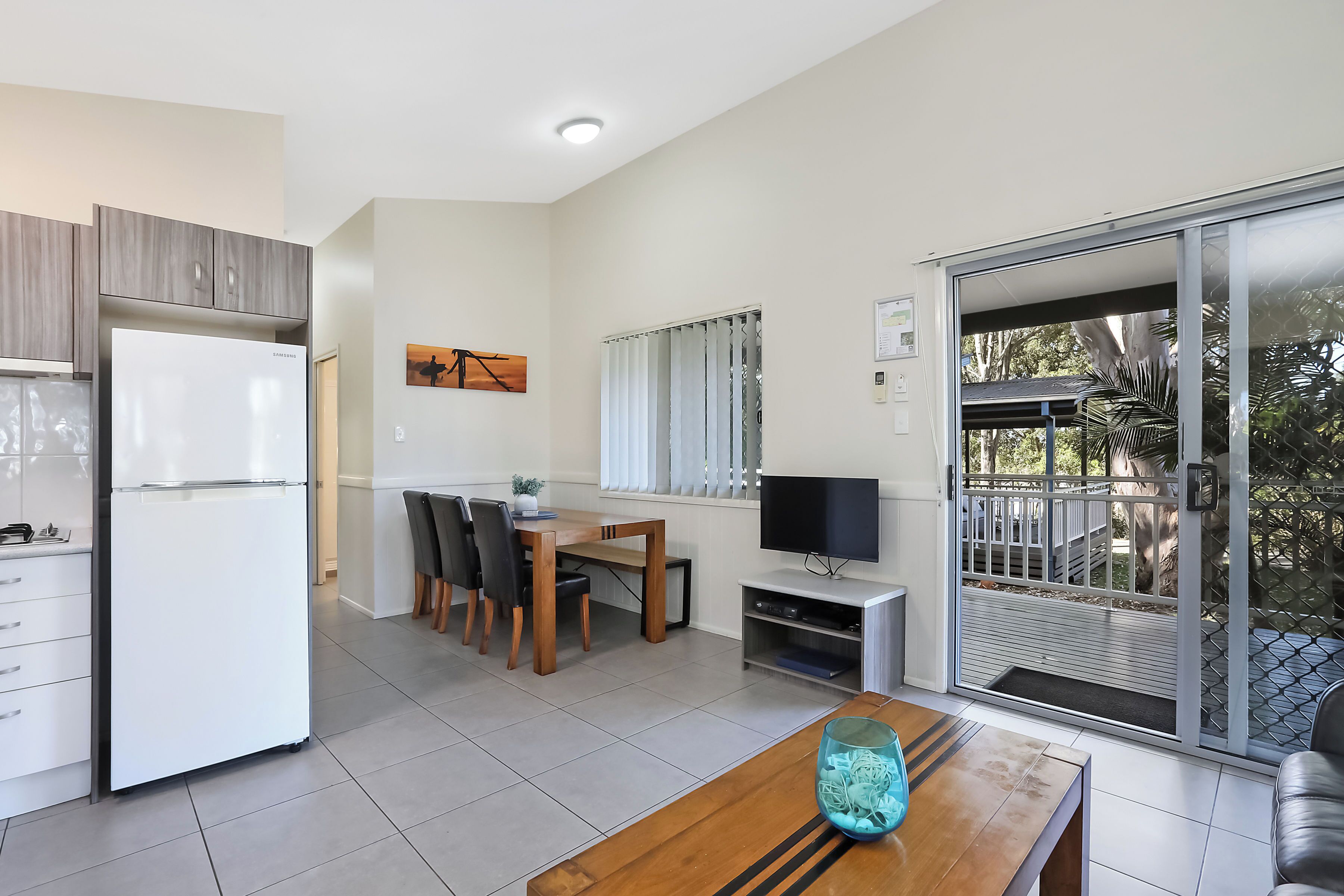 A modern kitchen with a refrigerator, dining table, chairs, and a TV.