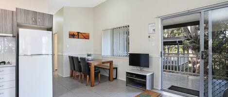 A modern kitchen with a refrigerator, dining table, chairs, and a TV.