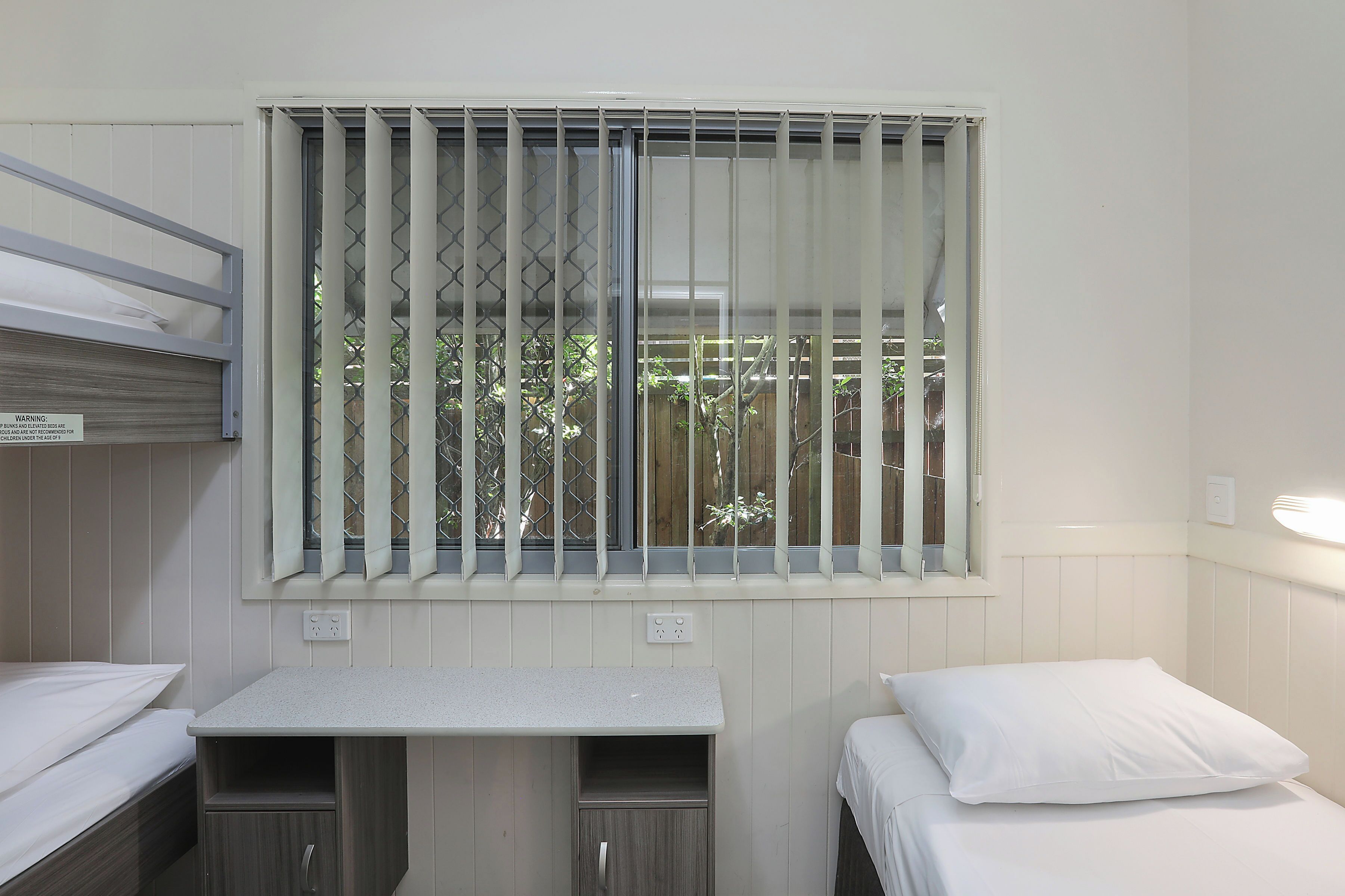 A small, clean room with a bunk bed, a desk, and a window with bars.