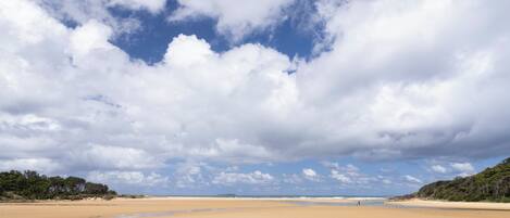 A wide sandy beach with a clear sky and some clouds.