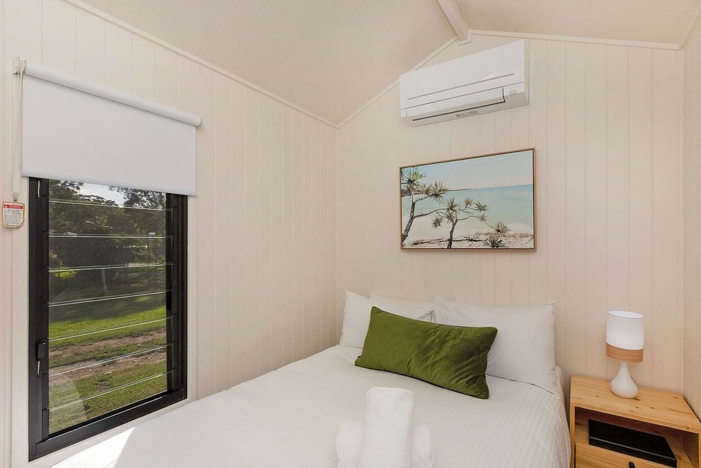 A bedroom with a bed, a green pillow, a white lamp, and an air conditioning unit.