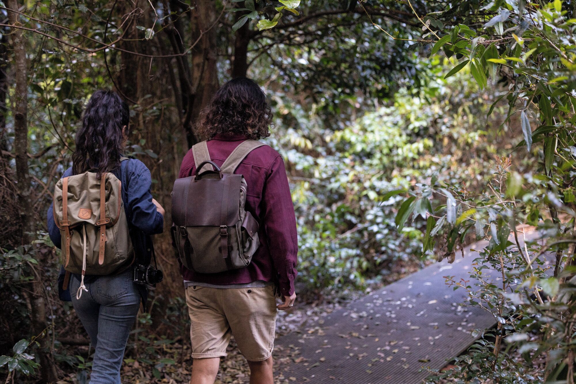 Two people walking on a forest path with backpacks.
