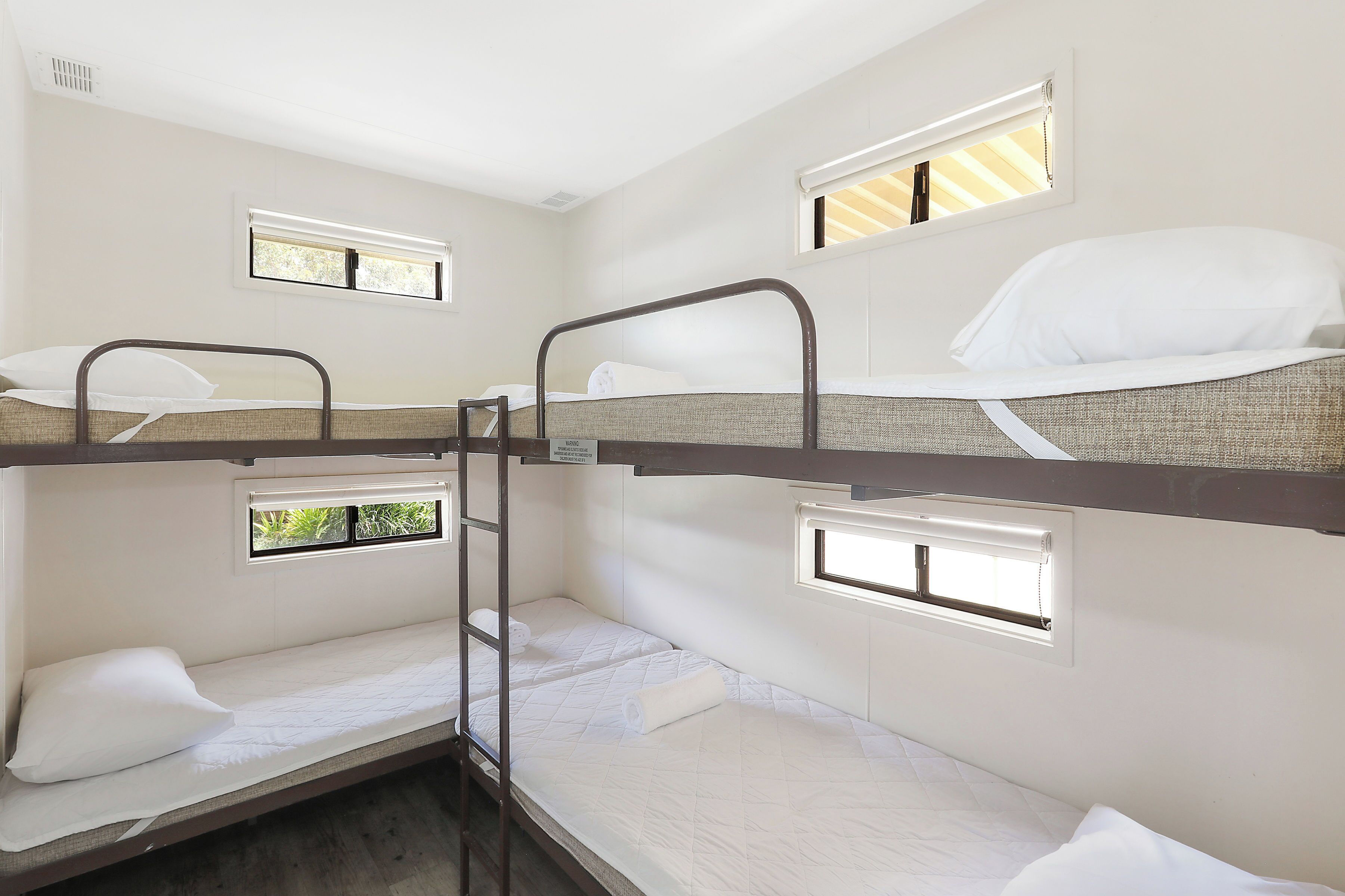 Une chambre avec deux lits superposés et deux fenêtres, chacune offrant une vue sur la verdure environnante.