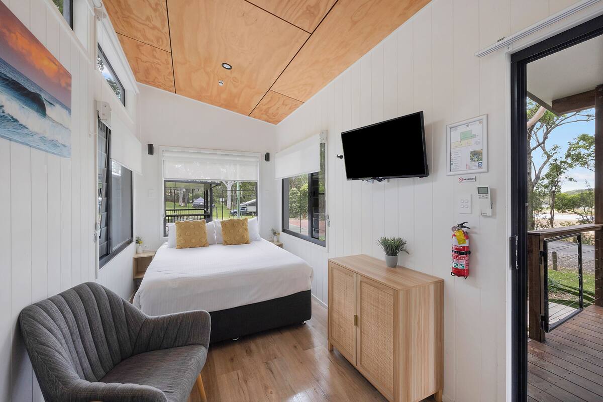 A modern bedroom with a large bed, a flat-screen TV, a wooden cabinet, and a fire extinguisher.