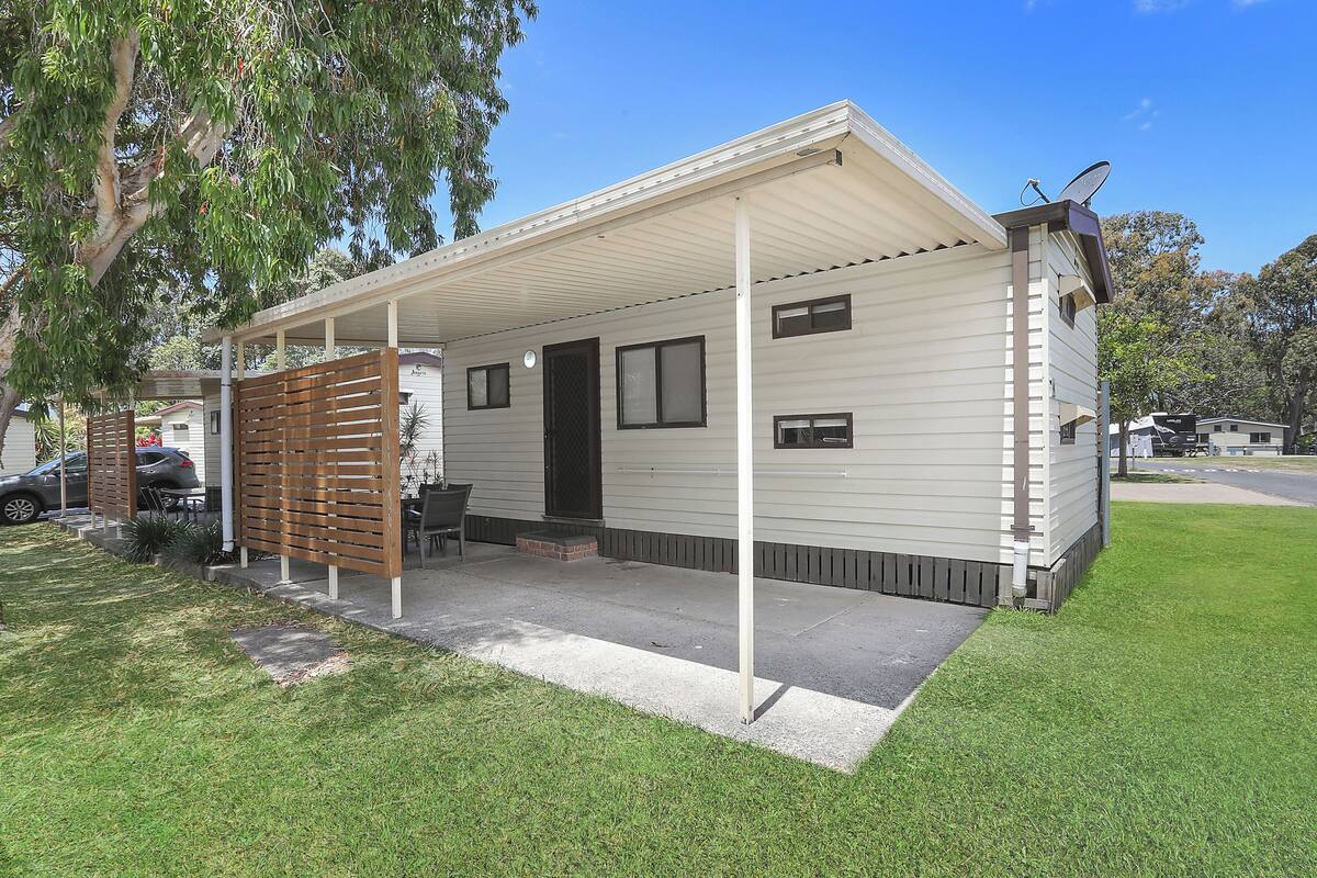 A single-story mobile home with a covered porch, a satellite dish, and a small front yard.