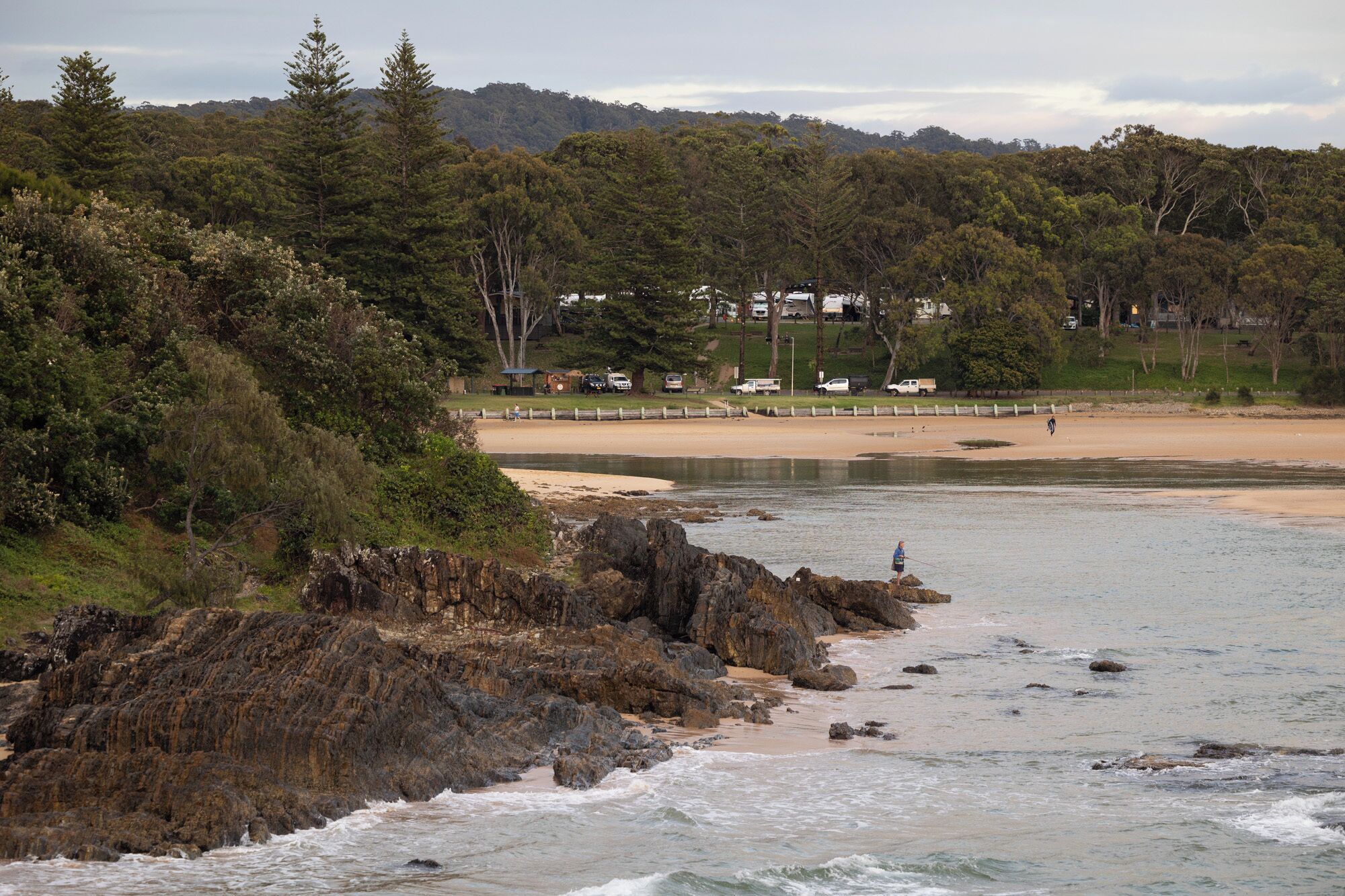 A coastal beach with rocky shoreline, a sandy beach, and a forested area in the background.