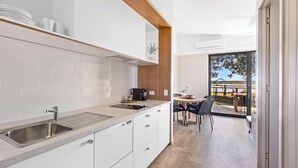 A modern kitchen with white cabinetry, a stainless steel sink, and a wooden countertop. There is a dining area with a table and chairs, and a view of a balcony with outdoor furniture. - Reflections Urunga - Holiday Park (Urunga)