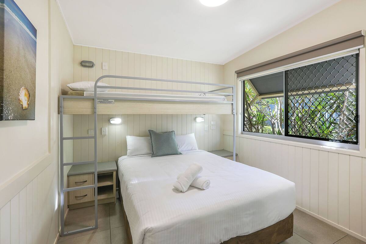 A bunk bed room with a window view, a bedside table, and a wall-mounted shelf.