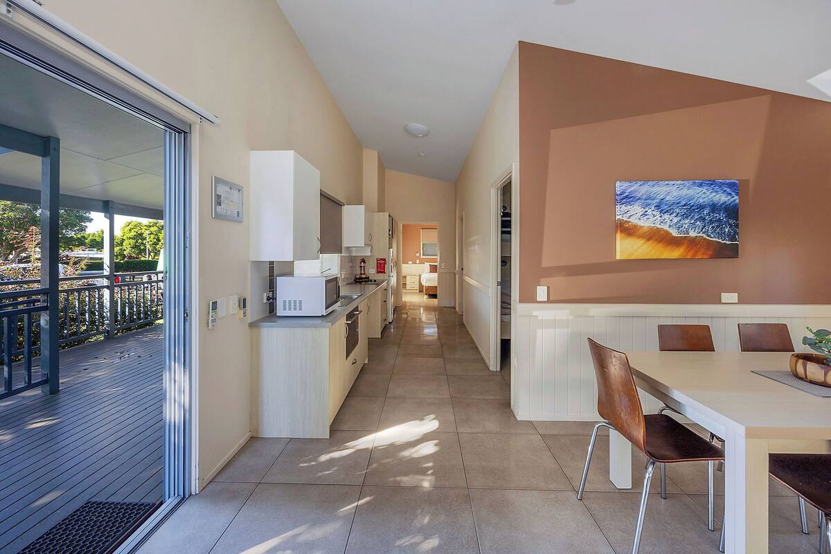 A modern kitchen with white cabinets, a dining area with a large table and chairs, and a view of the outdoors through a sliding glass door.