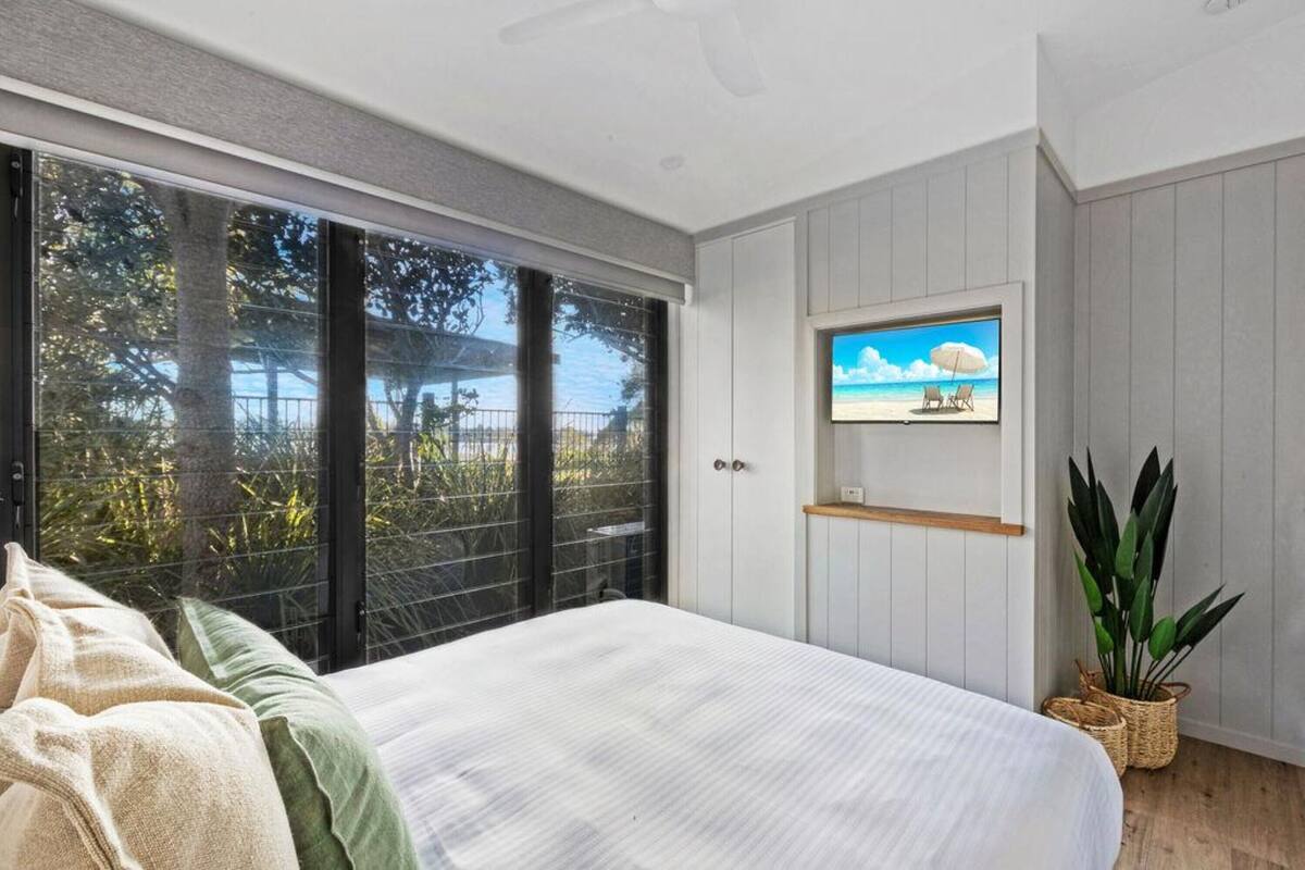 A bedroom with a large bed, a TV mounted on the wall, and a view of the outdoors through a sliding door.